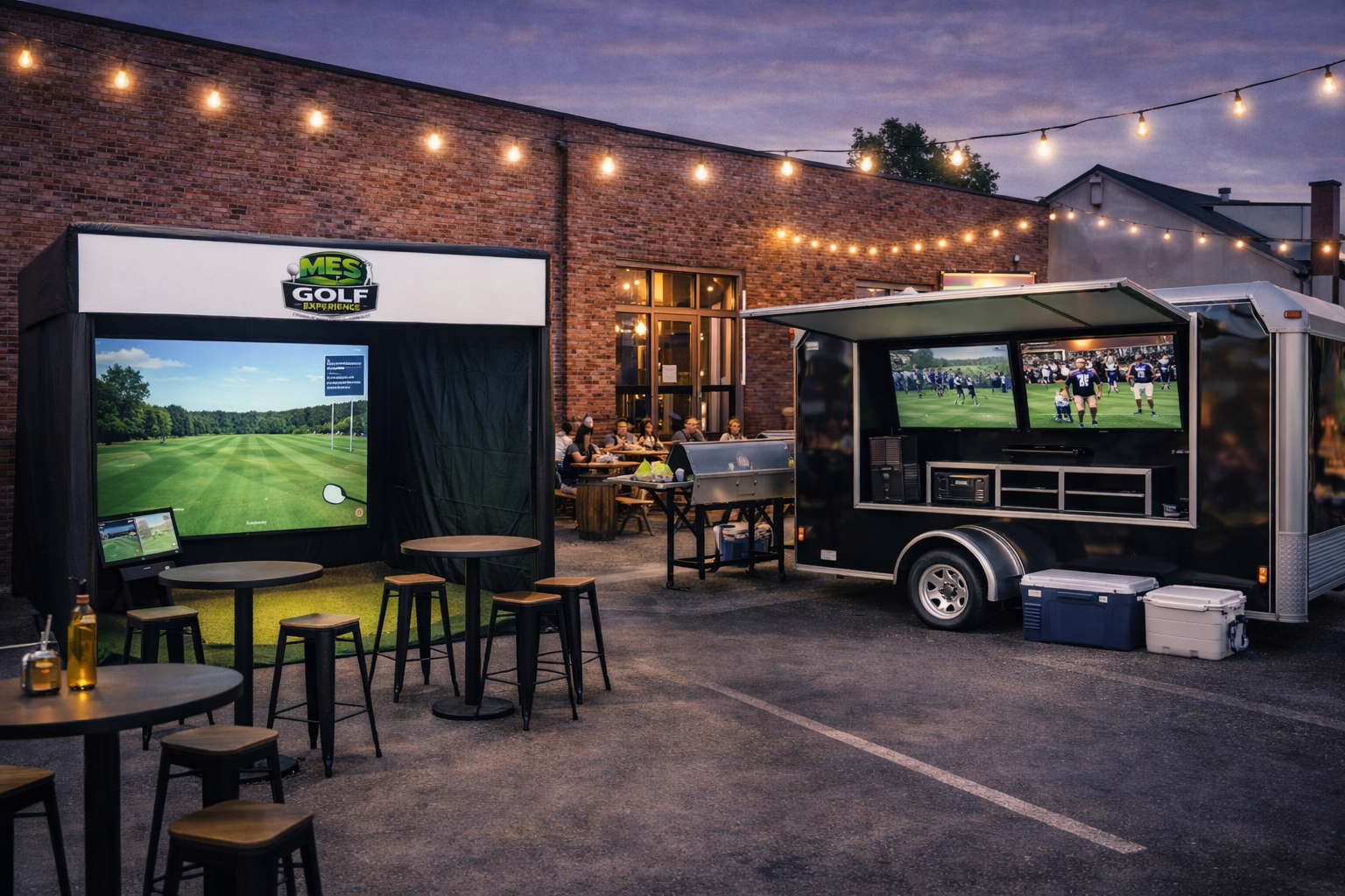 Outdoor scene with a mobile golf simulator setup, including a large projection screen displaying a golf course and a trailer with screens showing a football game, outdoor dining area with people, string lights overhead, and a brick building in the background at dusk.