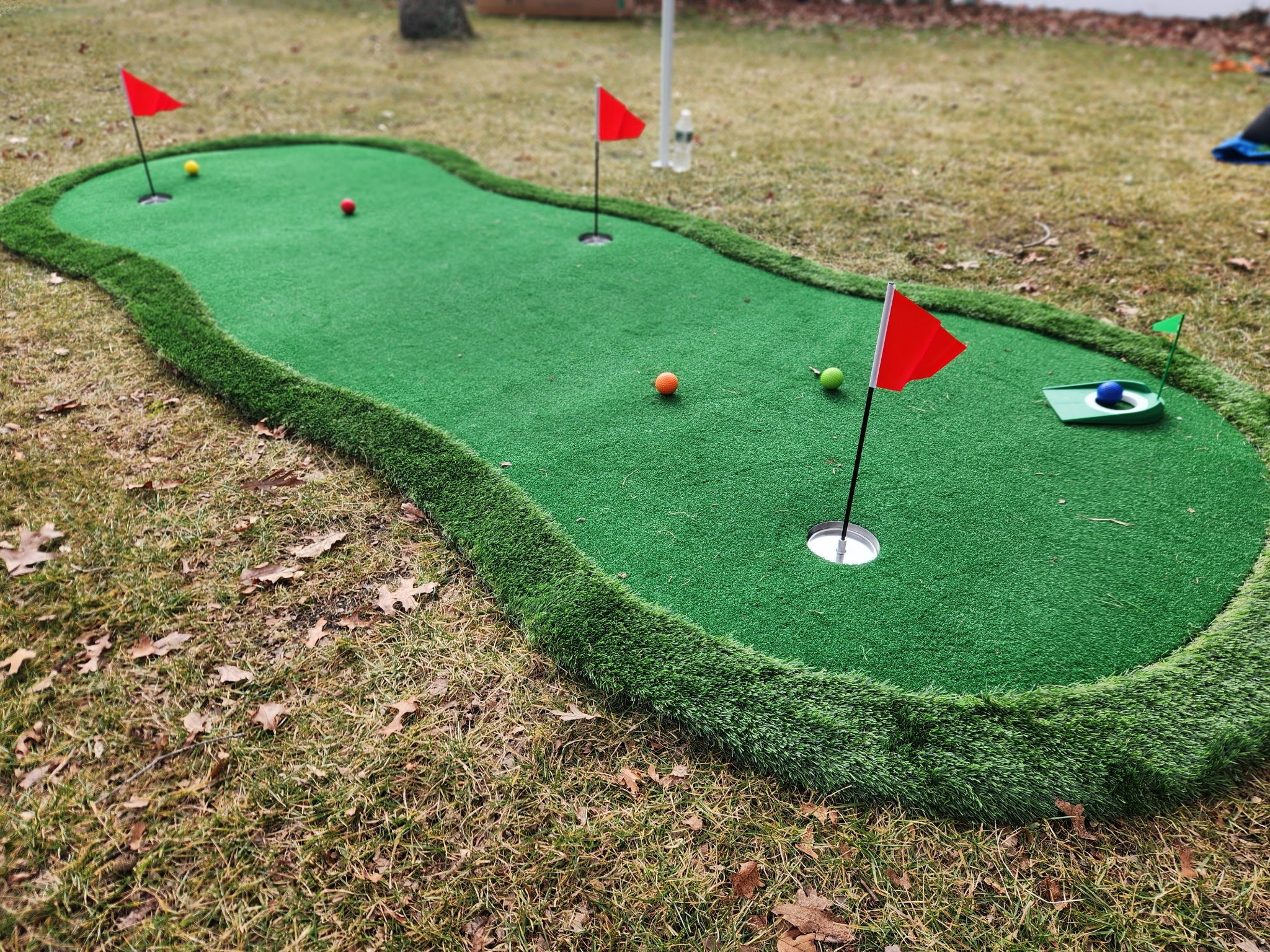 Miniature golf putting green with flags and golf balls on a grassy outdoor area.