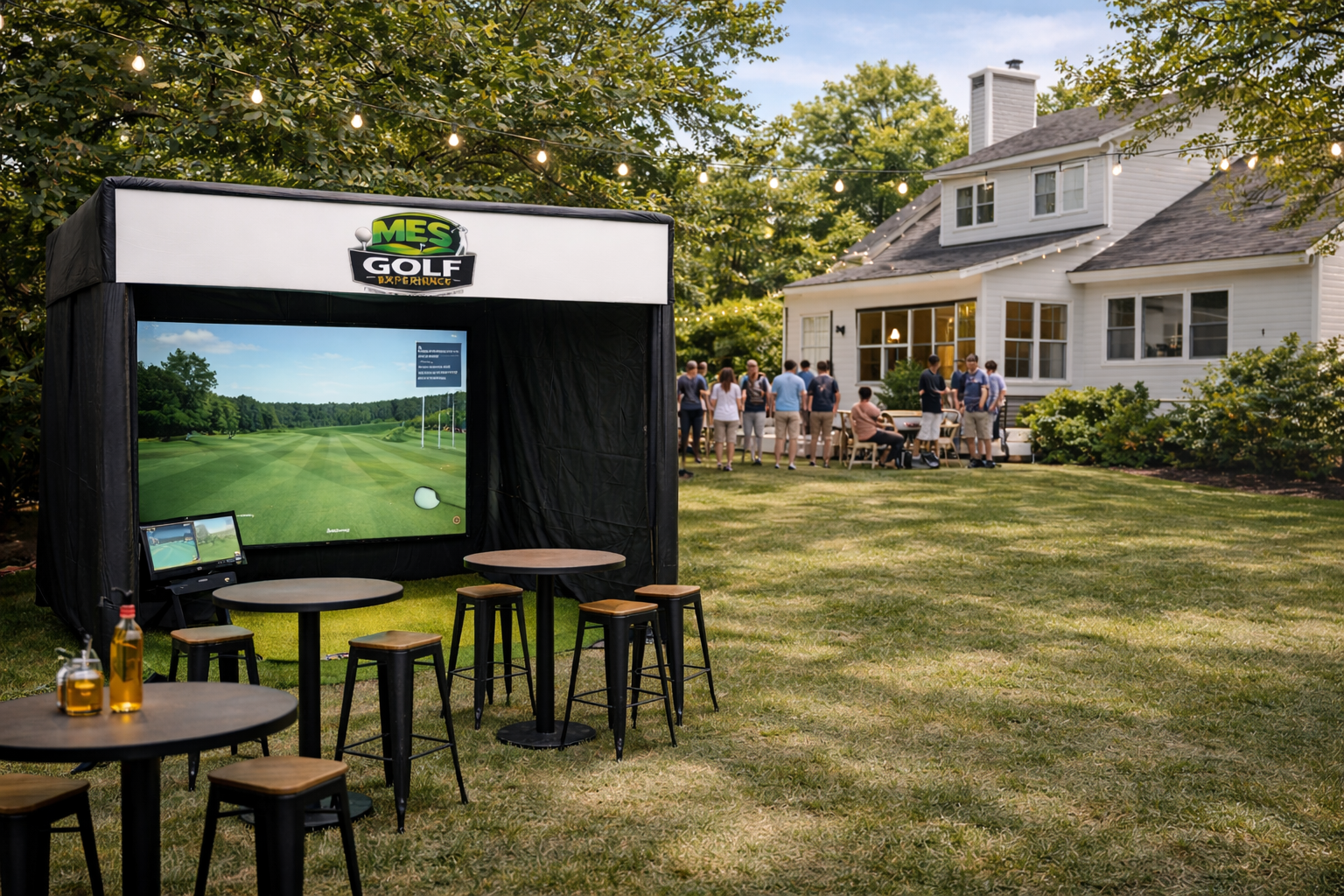 An outdoor gathering with people near a white house, with a large screen for virtual golf under a black canopy labeled MES Golf Performance, with small tables and stools nearby, on a well-maintained lawn surrounded by trees and string lights.