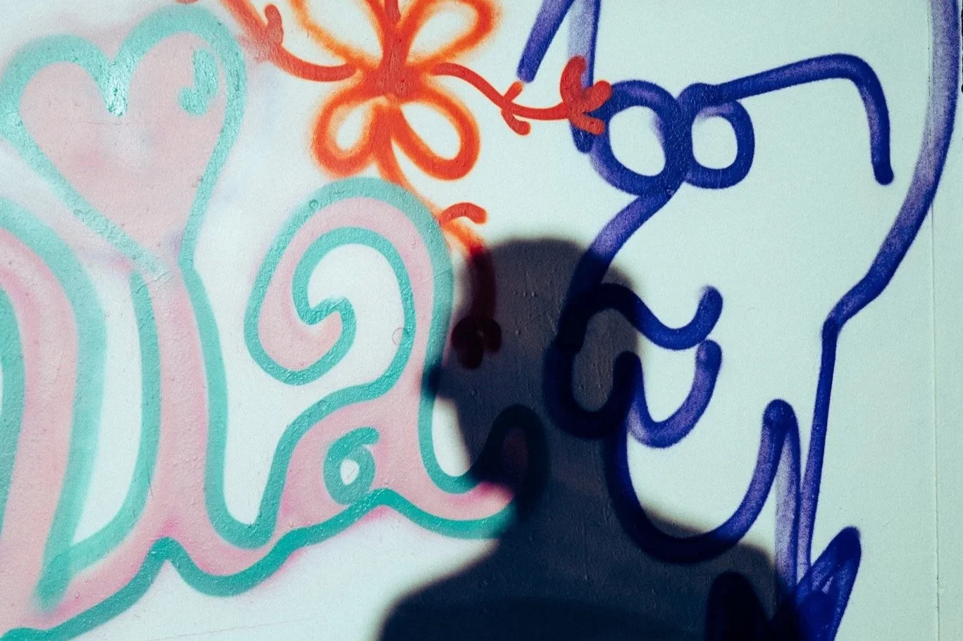 Children's colorful graffiti art on a wall featuring hearts, swirls, and abstract shapes in pink, blue, and red, with a shadow cast on the artwork.
