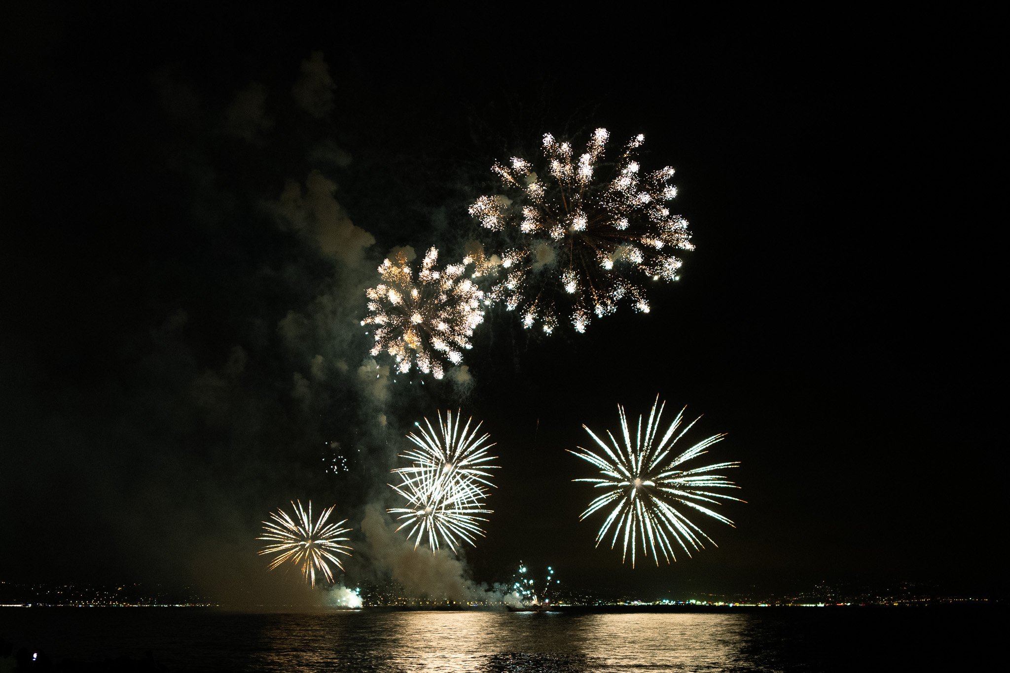 Fireworks display over a body of water at night with reflections on the surface.