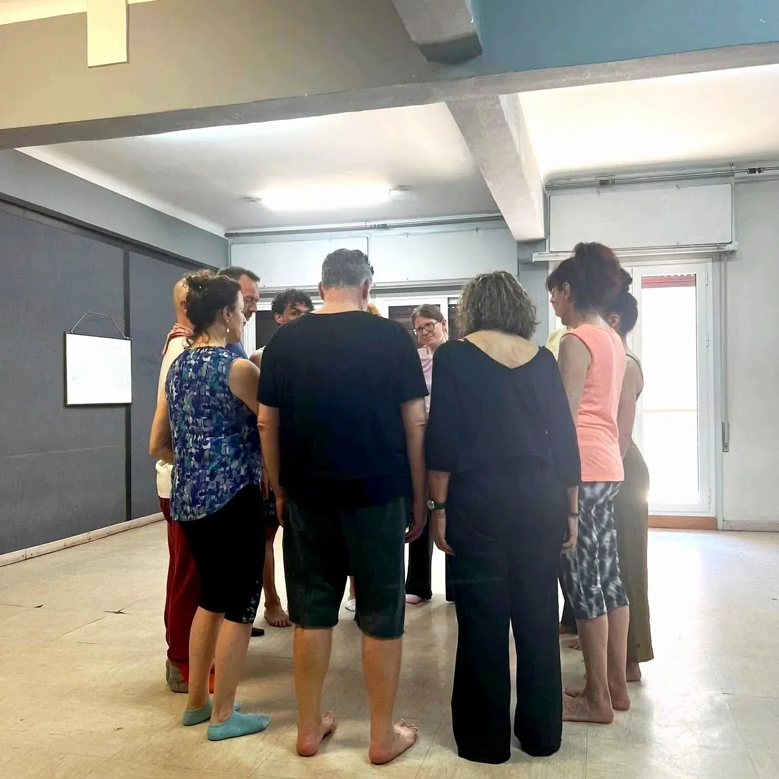 Group of people standing in a circle in an room with gray walls and a partially open door letting in bright light.