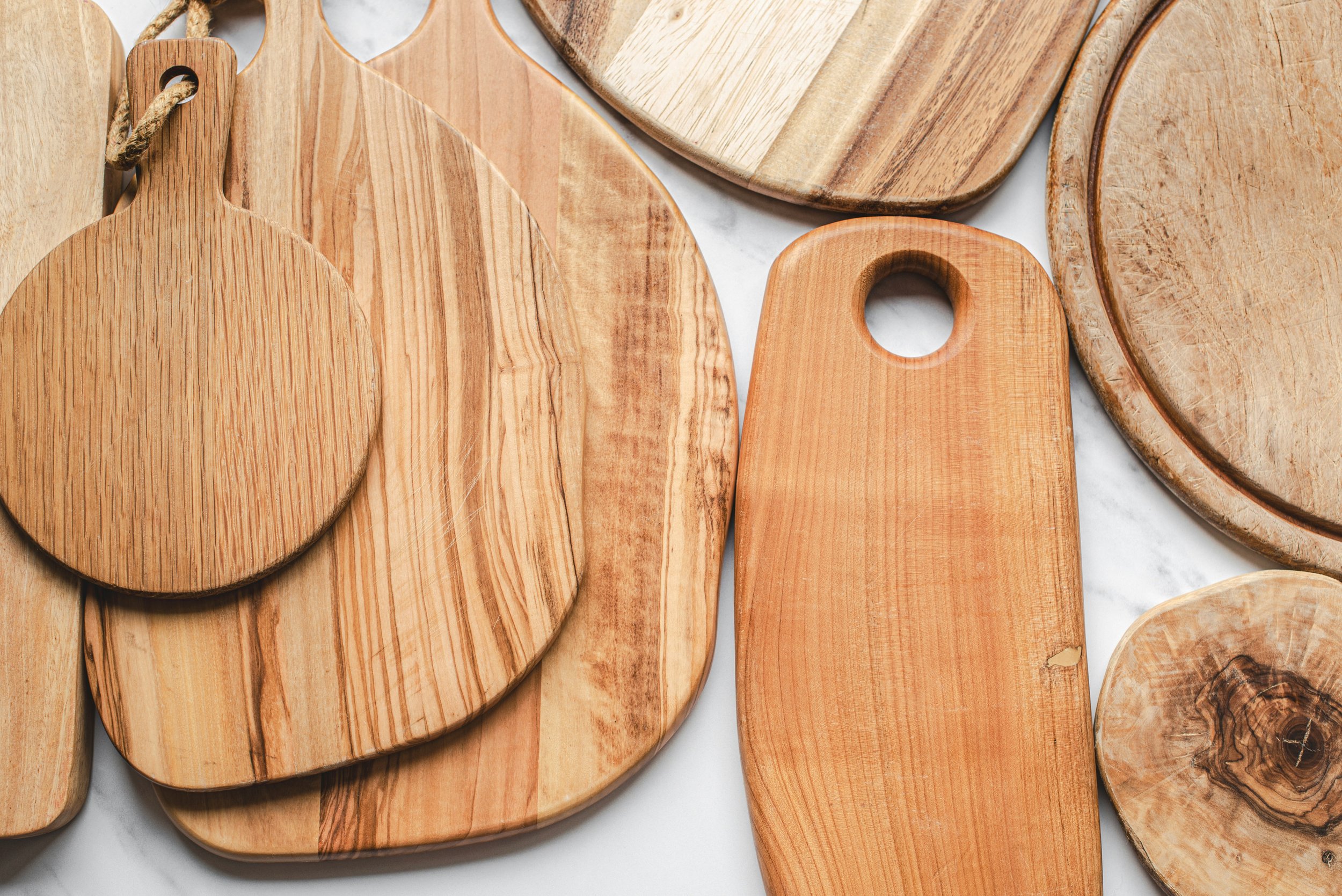 Various wooden cutting boards of different shapes and sizes stacked and arranged on a white surface.