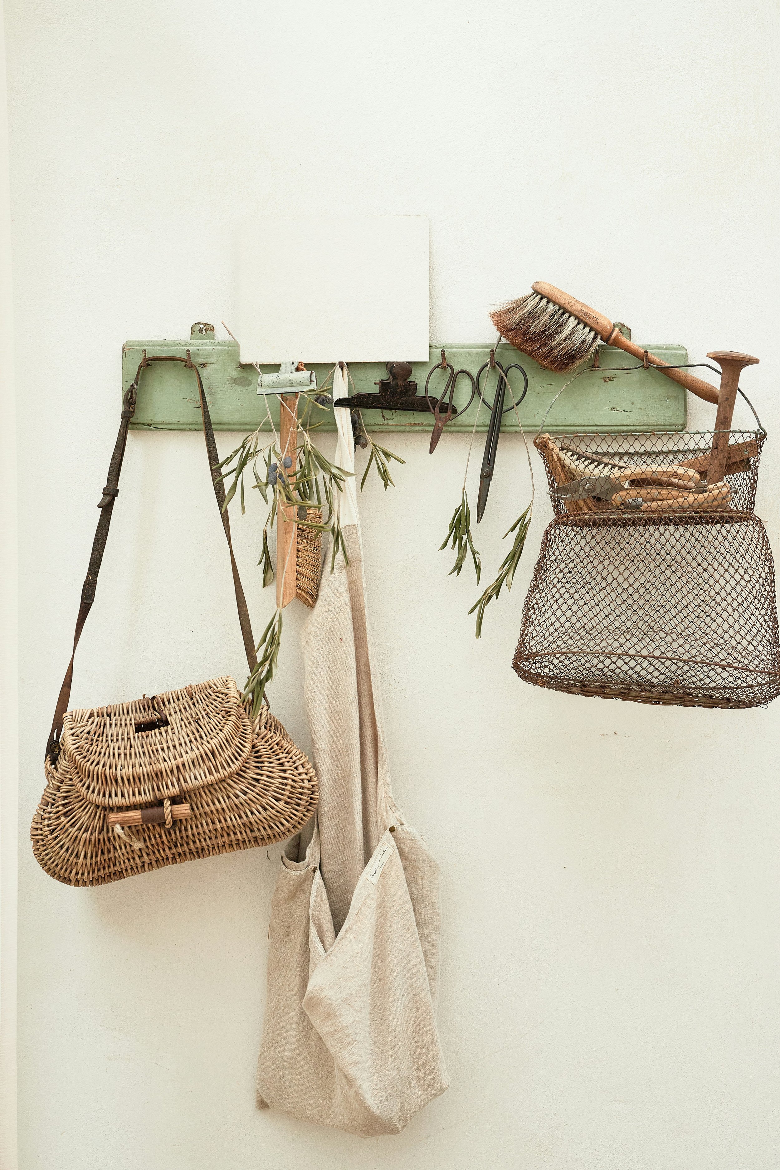 Wall-mounted organization with gardening tools, a woven bag, hanging greenery, and a basket with gardening supplies.