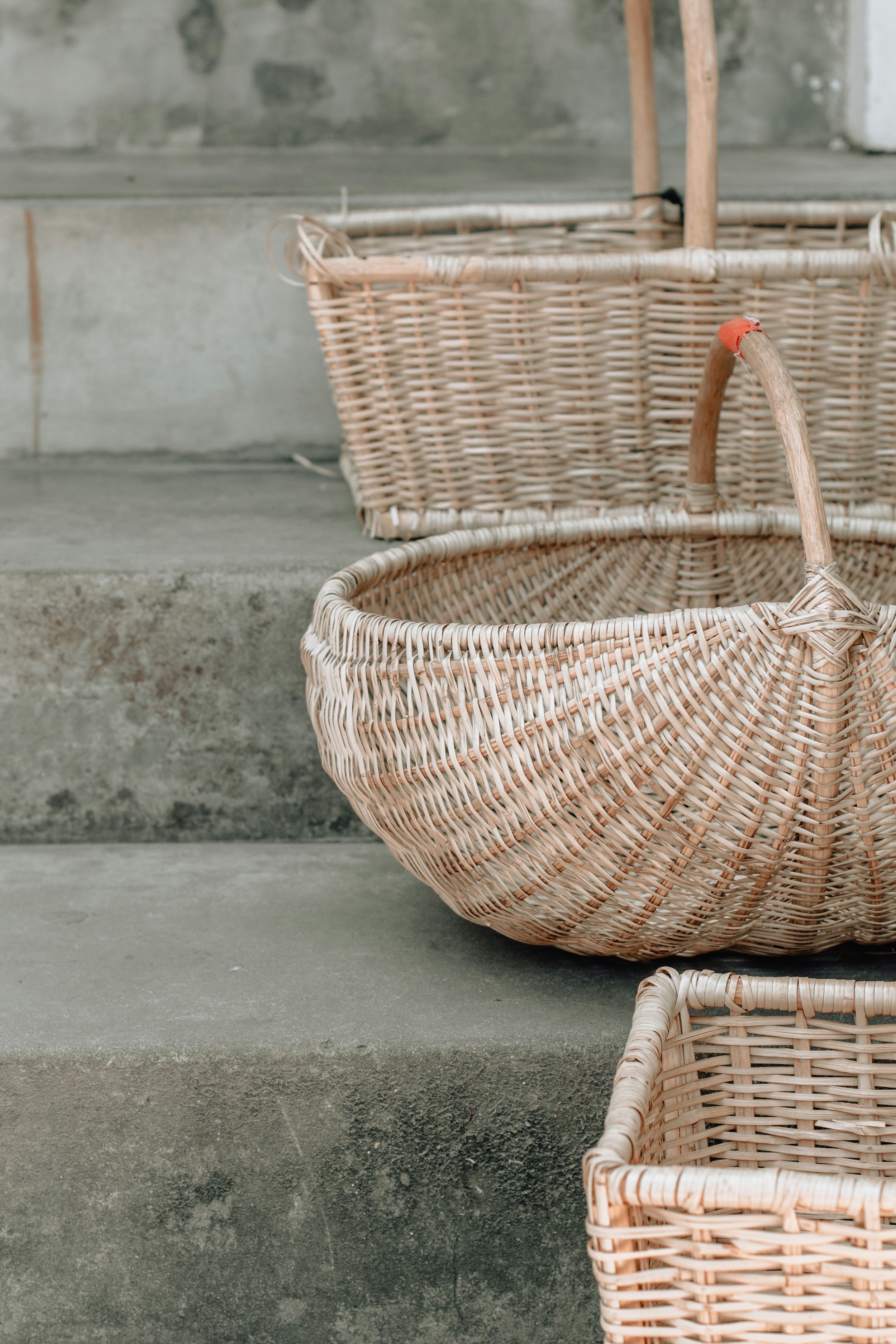 Three woven baskets of different sizes on concrete steps, with a weathered wall in the background.