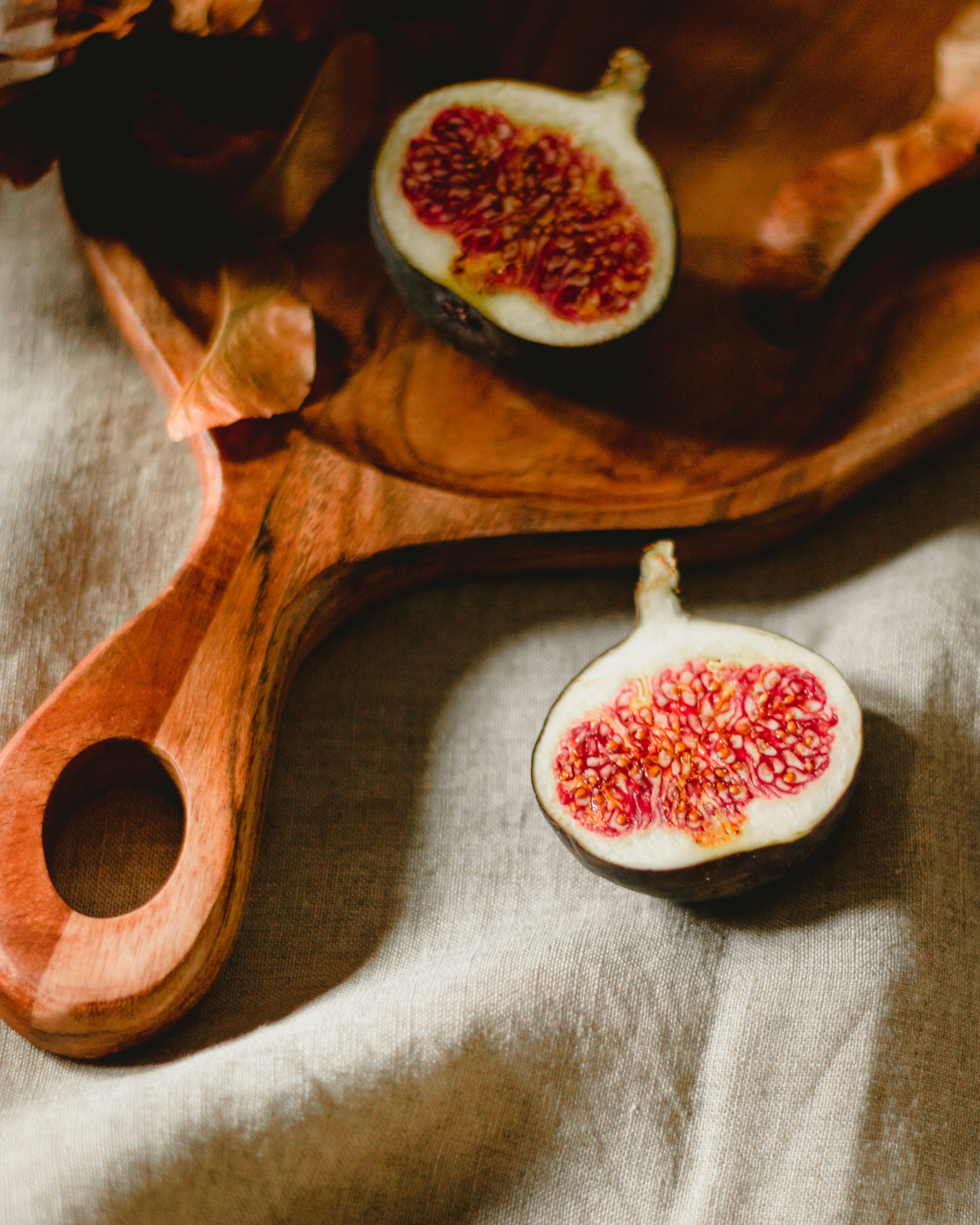 Halved fresh figs on a wooden serving platter on a beige cloth background.
