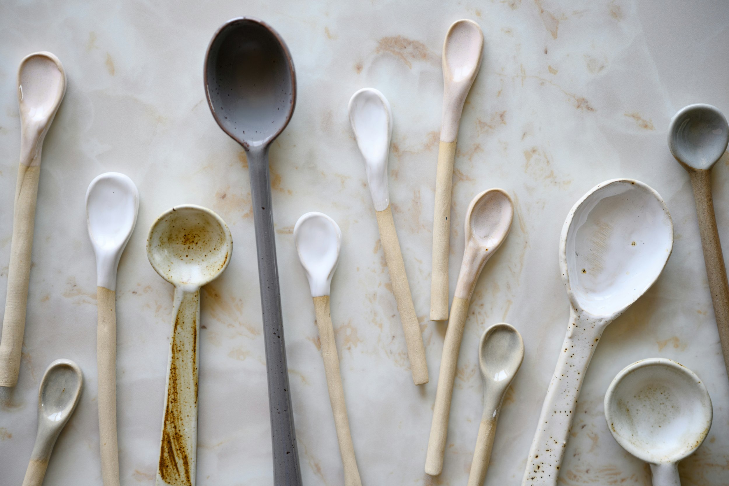 Assorted ceramic and wood spoons arranged on a marble surface, varying in size and color from beige to dark gray.