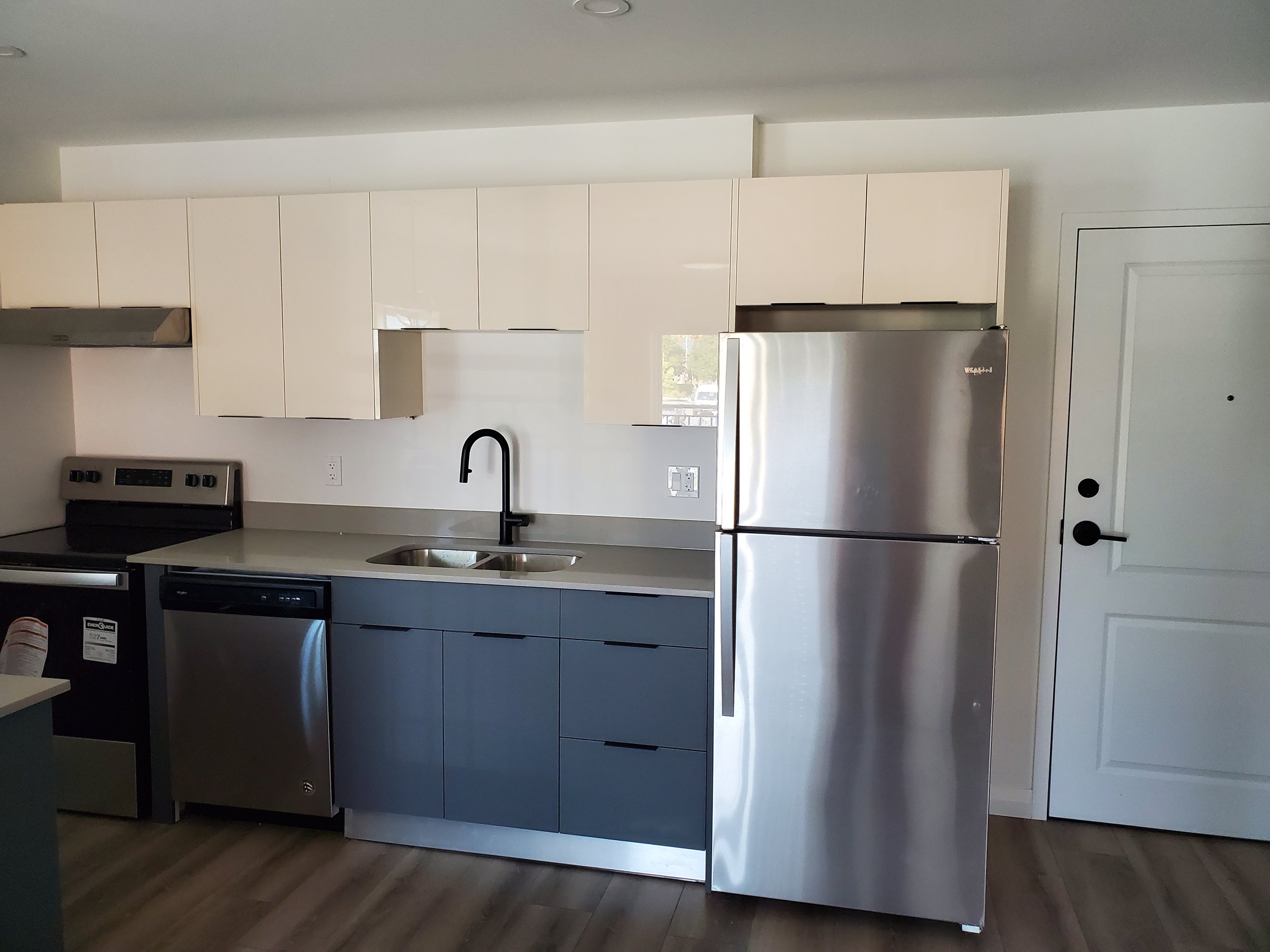 Modern kitchen with stainless steel appliances, including a refrigerator, stove, and dishwasher. Cabinets are white and gray, with a black faucet over a double sink.