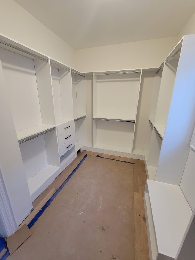Walk-in closet with white shelving and drawers, wood flooring protected by cardboard.
