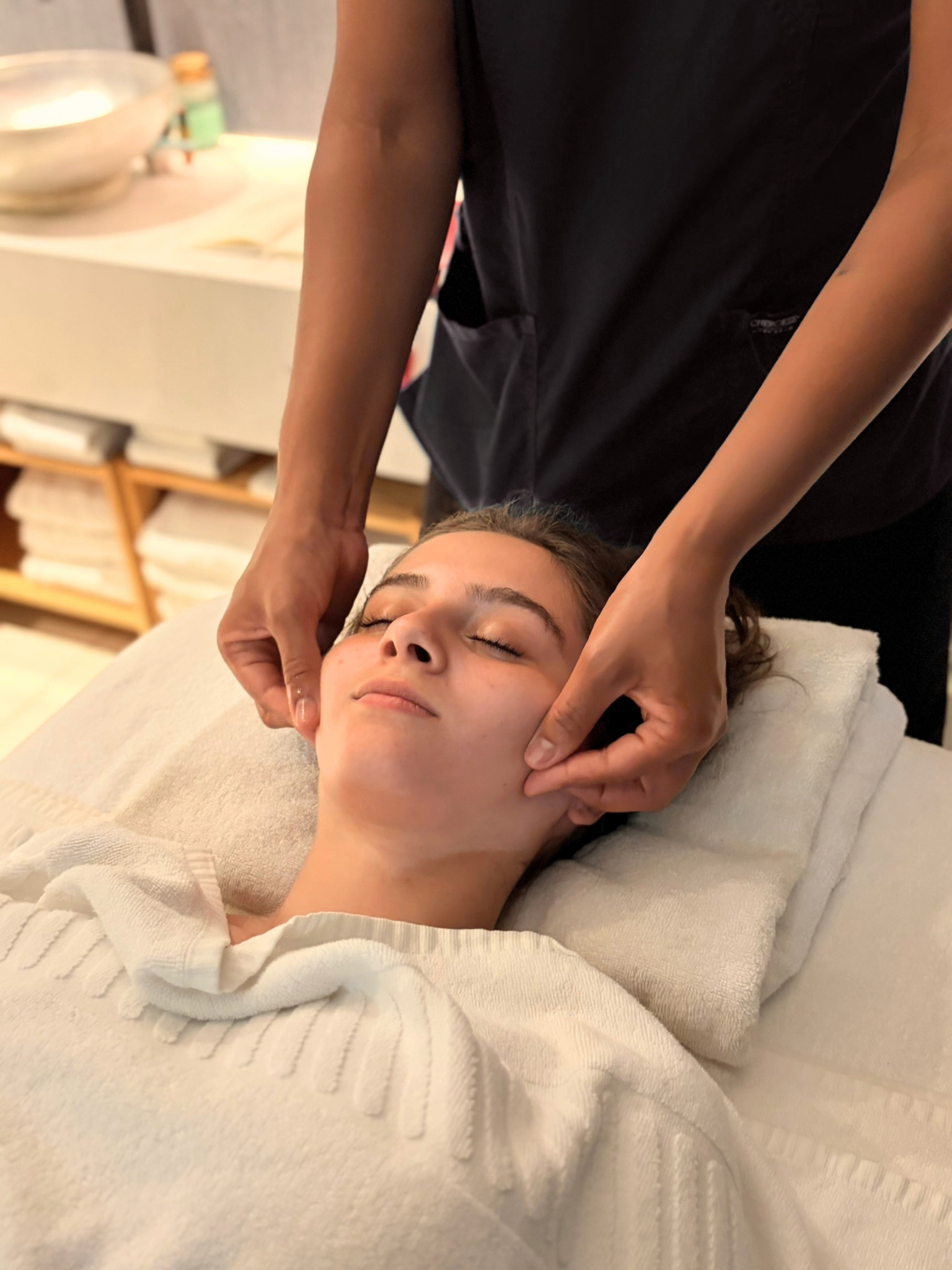 Pessoa recebendo massagem facial em uma cama, com expressão relaxada, em ambiente de spa ou clínica de estética
