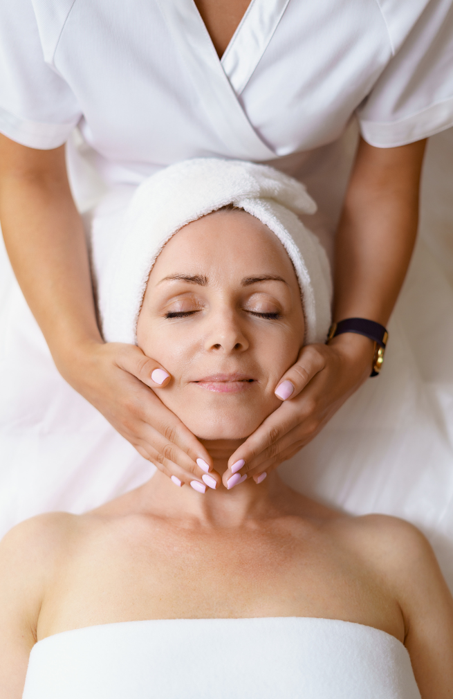 Pessoa recebendo massagem facial relaxante enquanto está deitada com uma toalha na cabeça