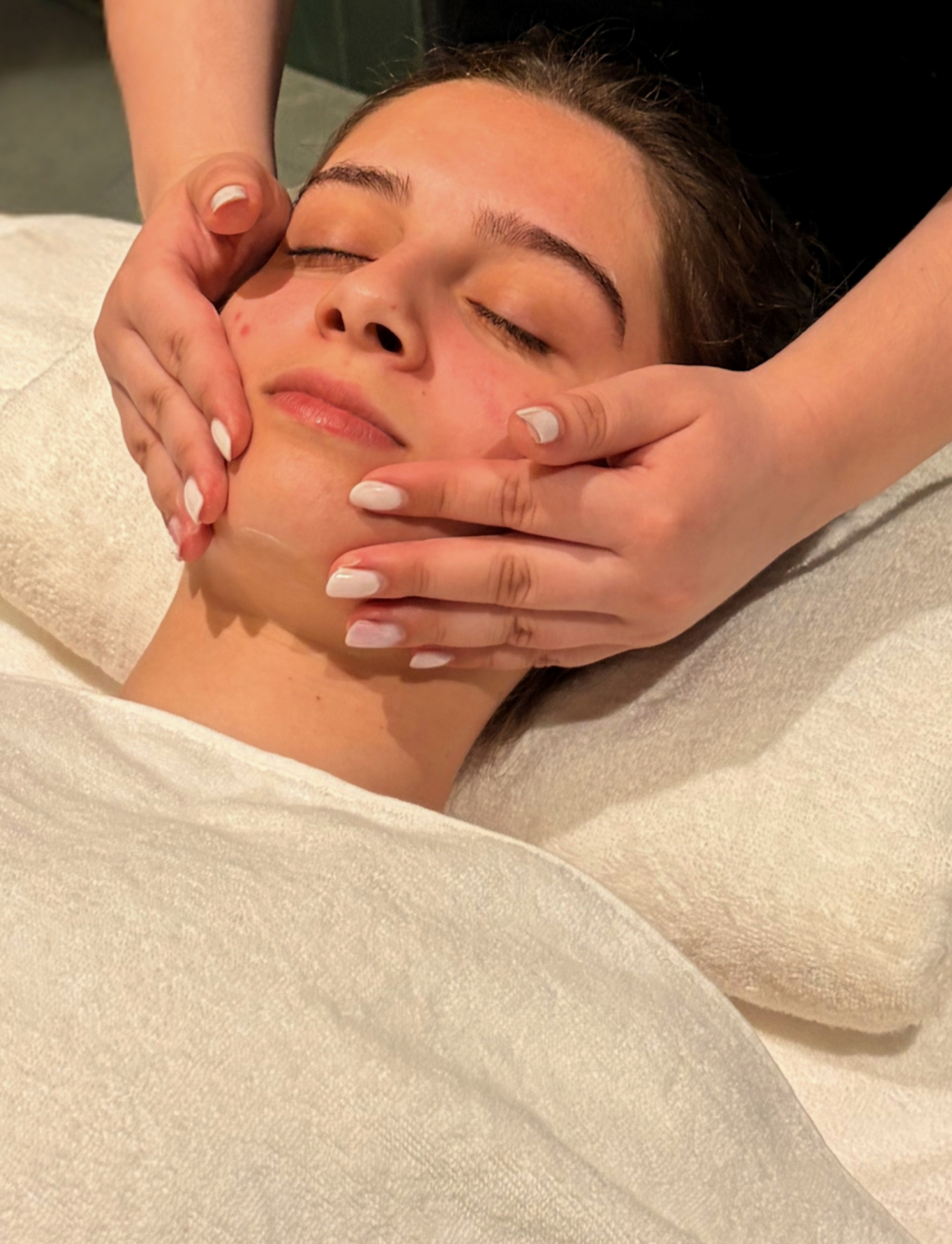 Pessoa recebendo uma sessão de massagem relaxante no rosto, com expressão tranquila, em ambiente de spa.