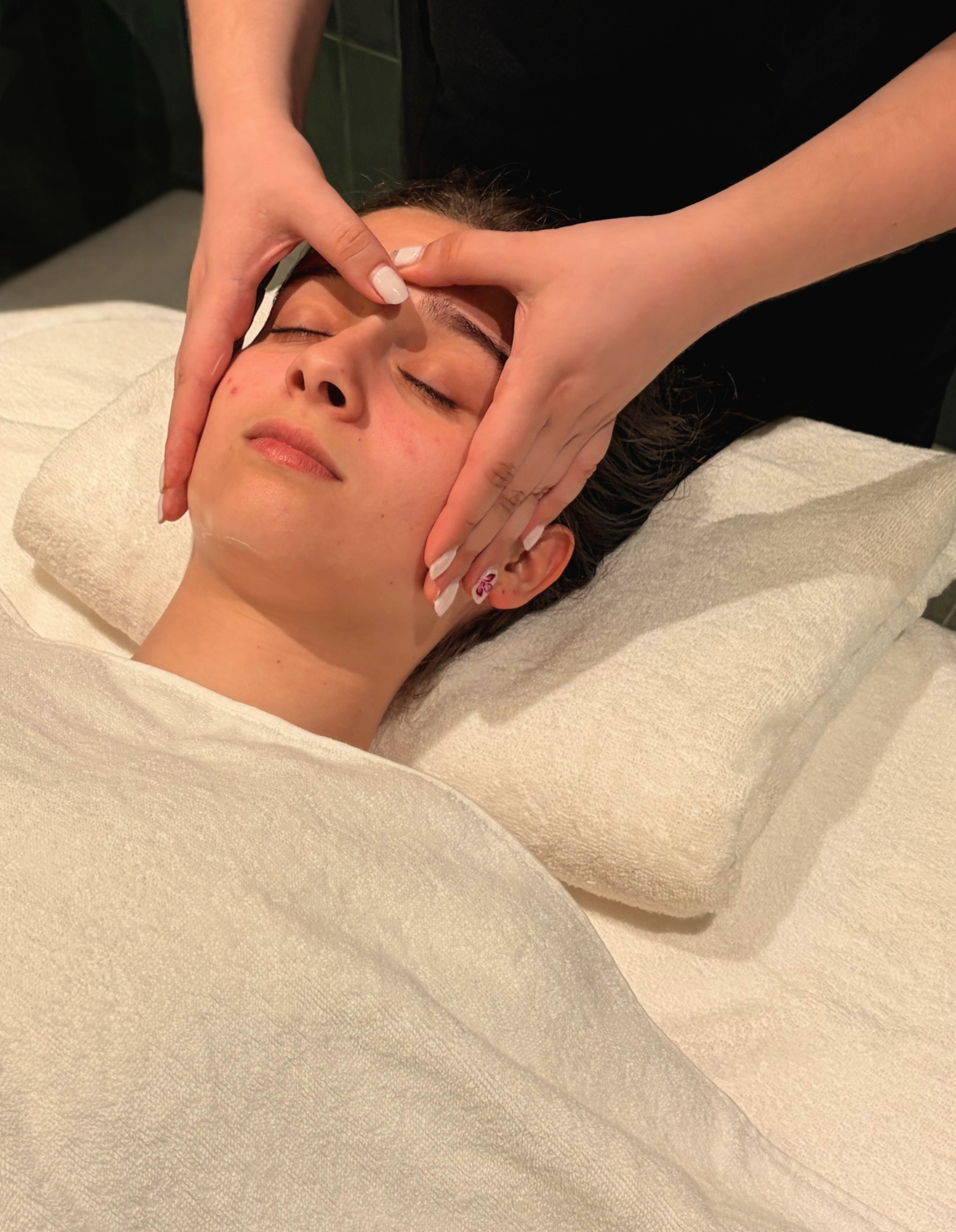Pessoa recebendo uma massagem relaxante na testa, deitada em uma cama ou massador.
