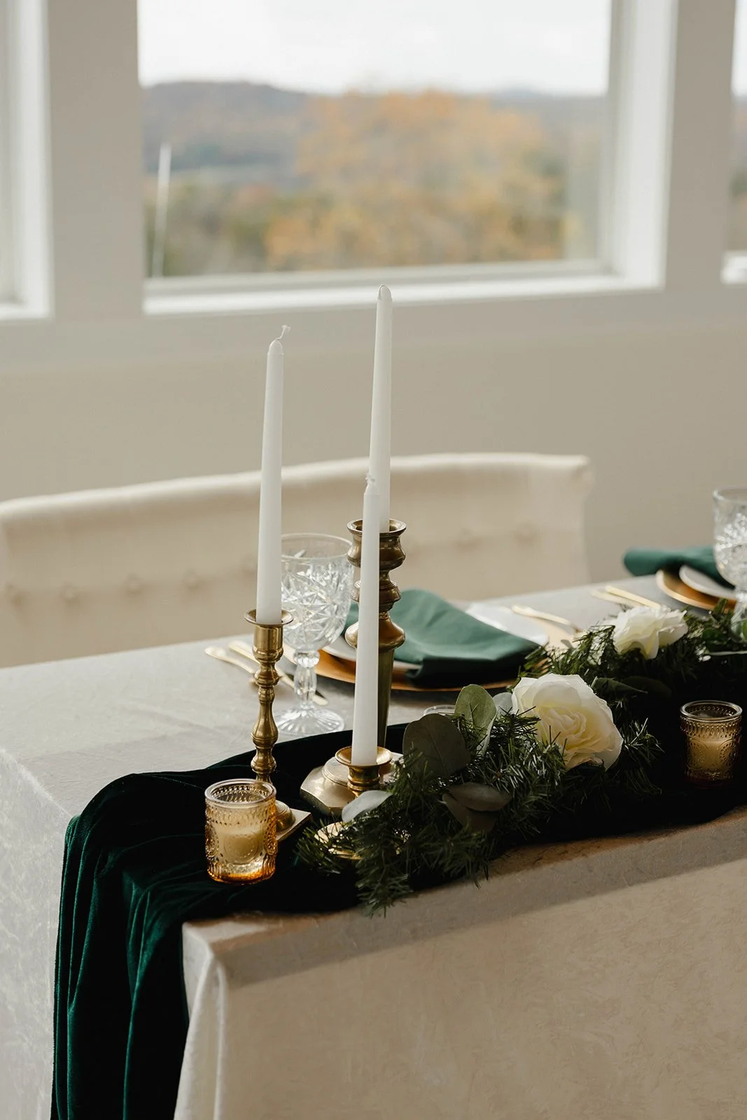 Wedding reception table styled with taper candles, gold holders, greenery garland, and soft neutral linens