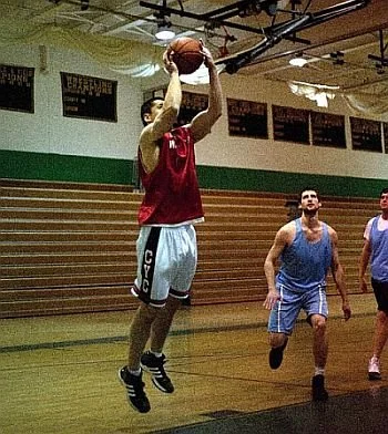 Image of Jeff Wu. A basketball player in a red jersey jumping to shoot the ball on an indoor court with two defenders nearby.