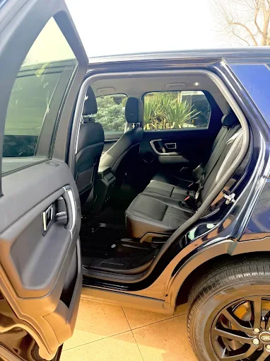 Open rear door of a black SUV showing the backseat area with black seats, headrests, and seatbelts inside.