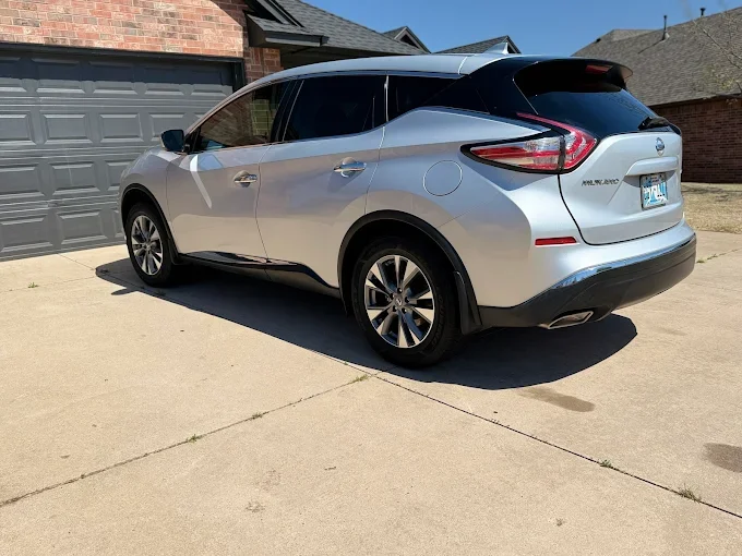 Silver Nissan Murano parked in a driveway in front of a garage on a sunny day.