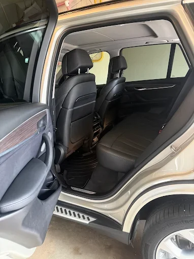 Interior of an SUV showing the back seat area with black leather seats and headrests, viewed from the open rear door.