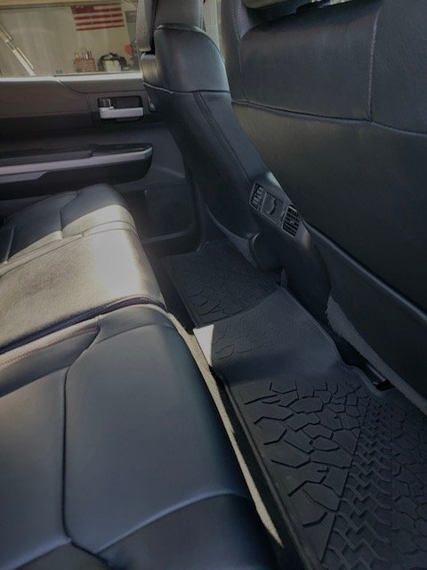 Backseat area of a vehicle showing black leather seats, floor mats, and back of the front seats with the window and door panel visible.