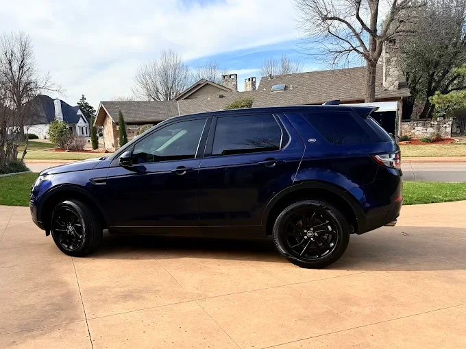 Black SUV parked on a driveway in a suburban neighborhood with houses and trees in the background.