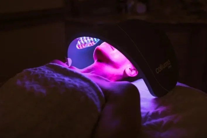 Person undergoing a purple LED light therapy session with their eyes closed, lying on a bed.