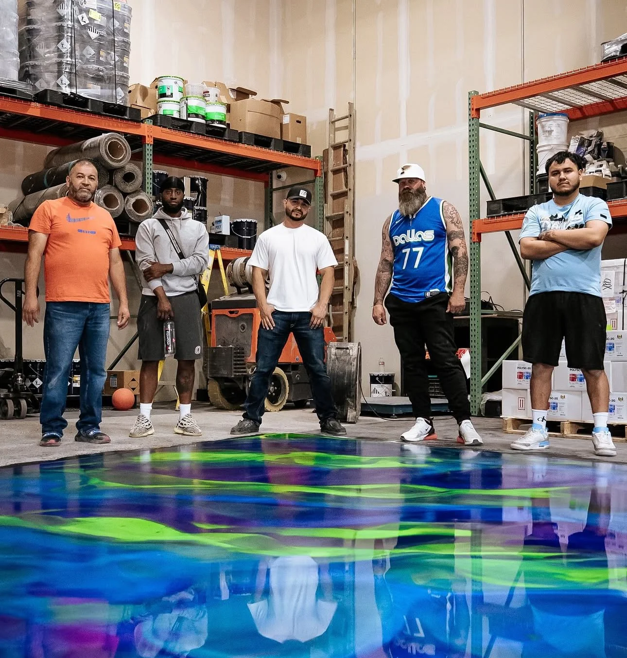 Five men standing in a warehouse with shelves of supplies, showcasing a colorful epoxy floor design.