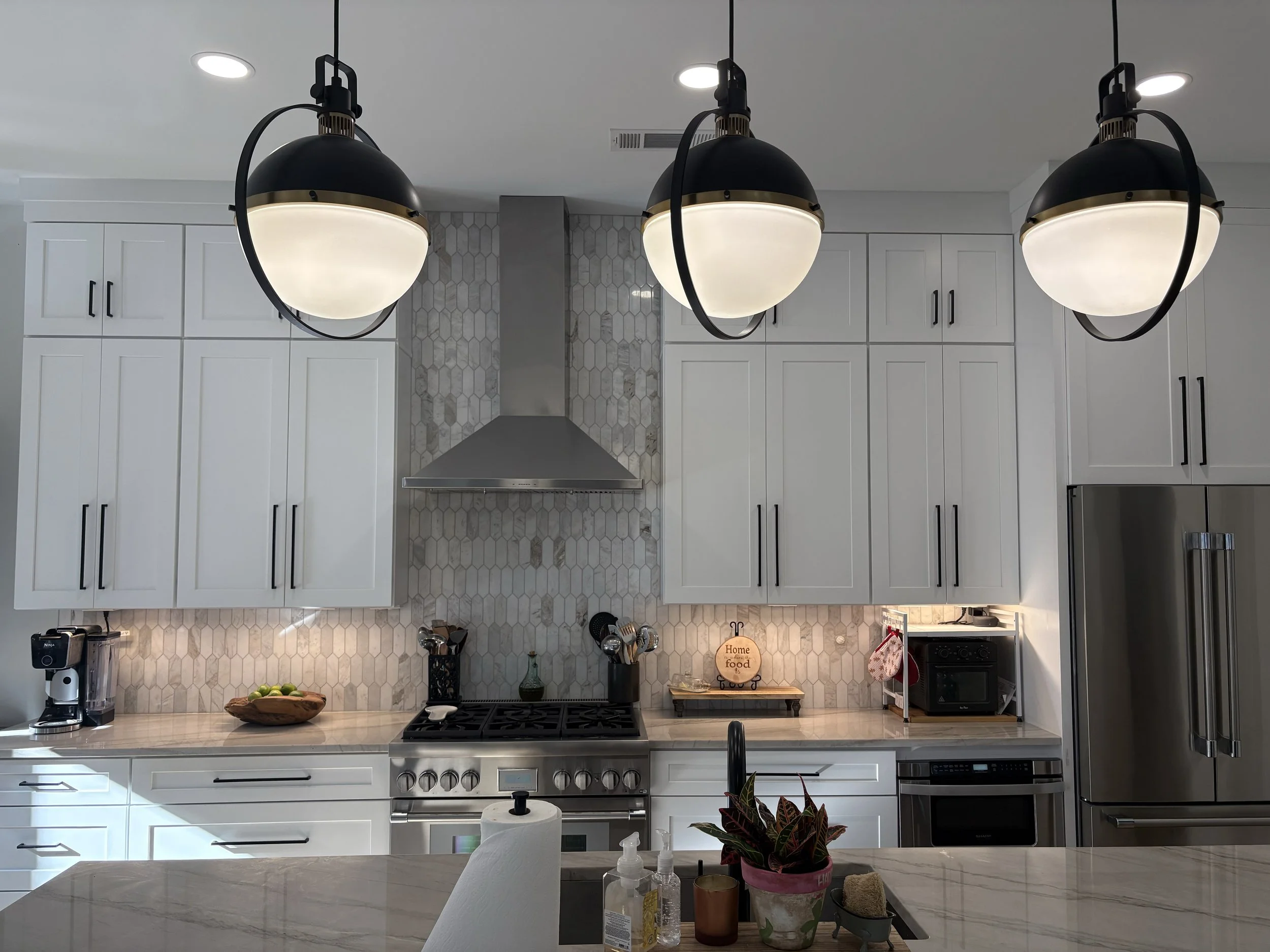 Modern kitchen with white cabinets, marble countertops, stainless steel appliances, pendant lights, and a hexagon tile backsplash.