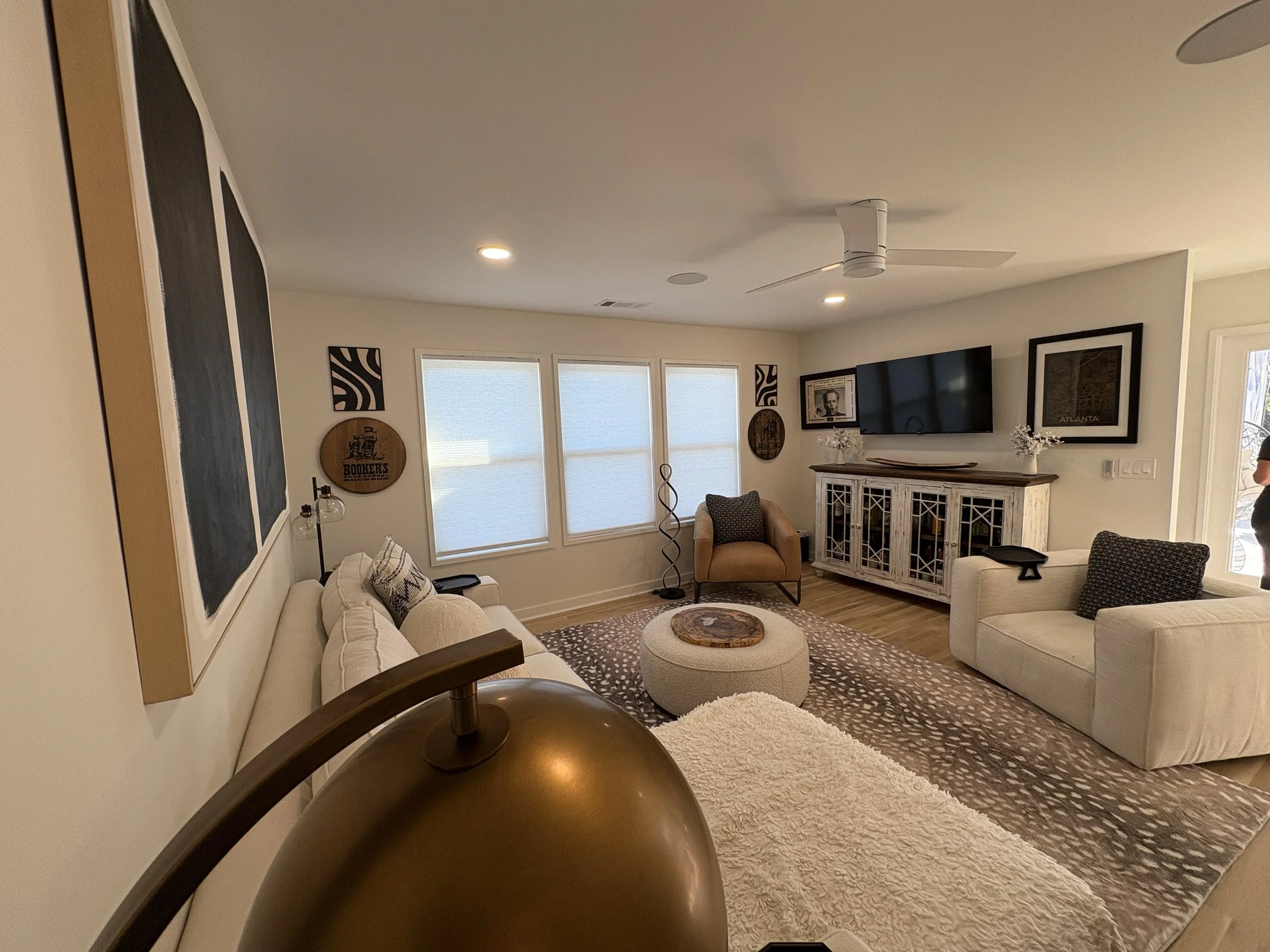 Living room with white sofas, patterned rug, armchair, TV, wall art, ceiling fan, windows with blinds, and decorative items.