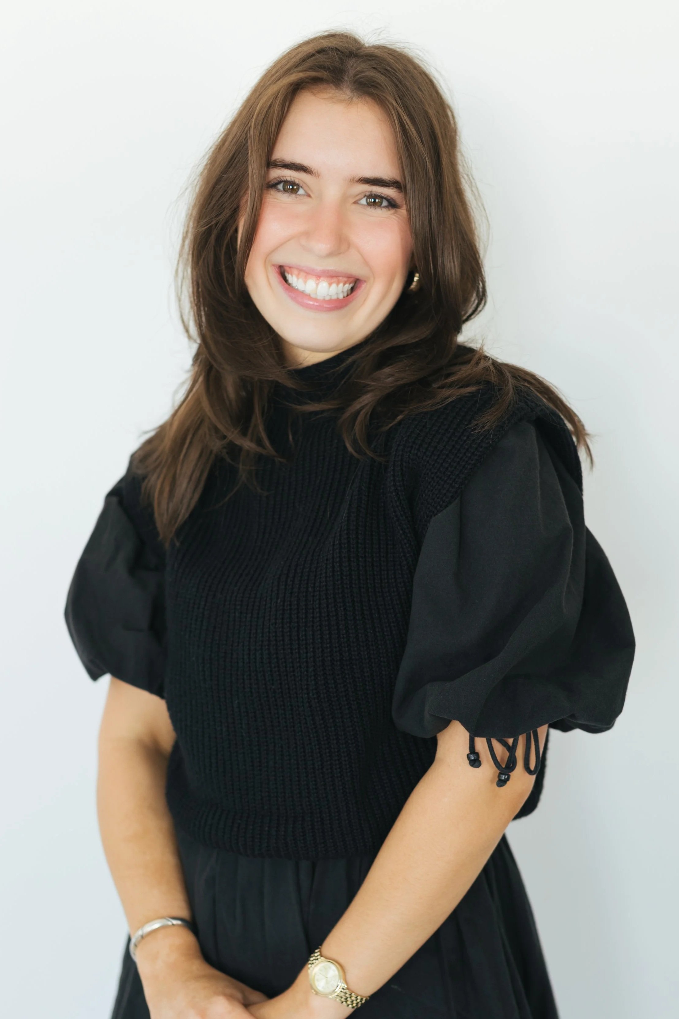 Katie Robertson, owner and lead planner of kg&co. with with long brown hair, sitting down, smiling, and wearing a black puff-sleeve mini dress.