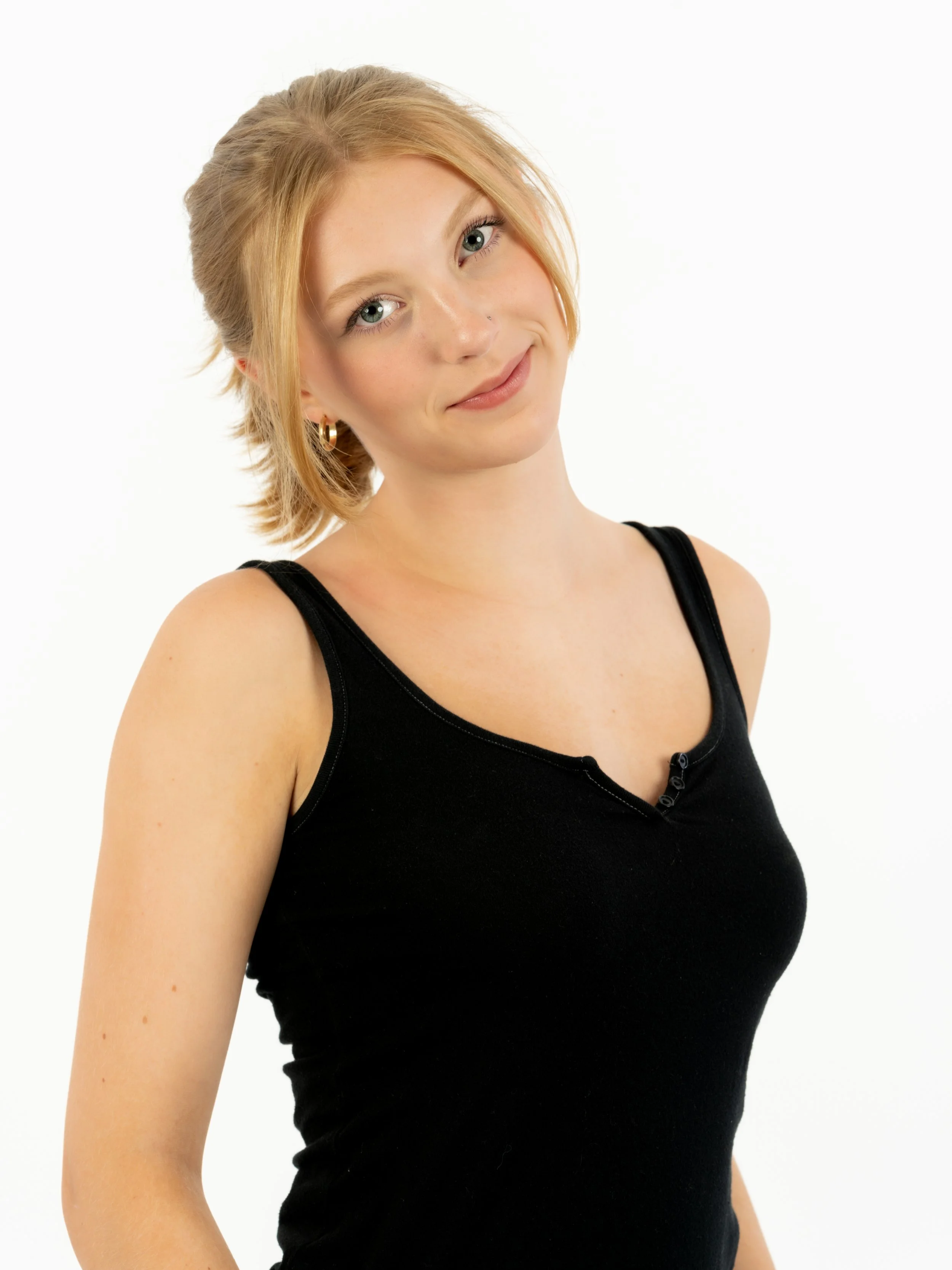 A young woman with shoulder-length blonde hair wearing a black sleeveless top with a slight smile, standing against a plain white background.