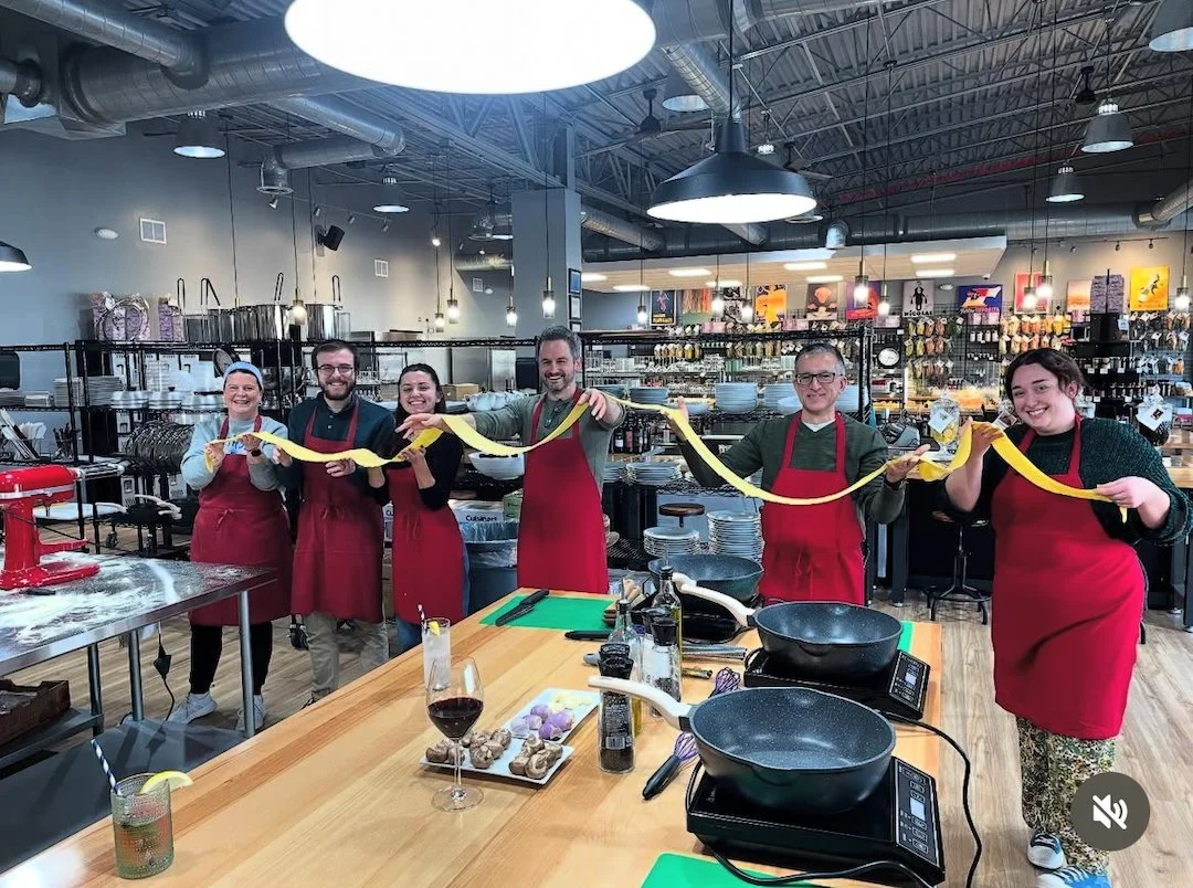 A group in red aprons stretching fresh pasta between them at The Local Epicurean in East Lansing