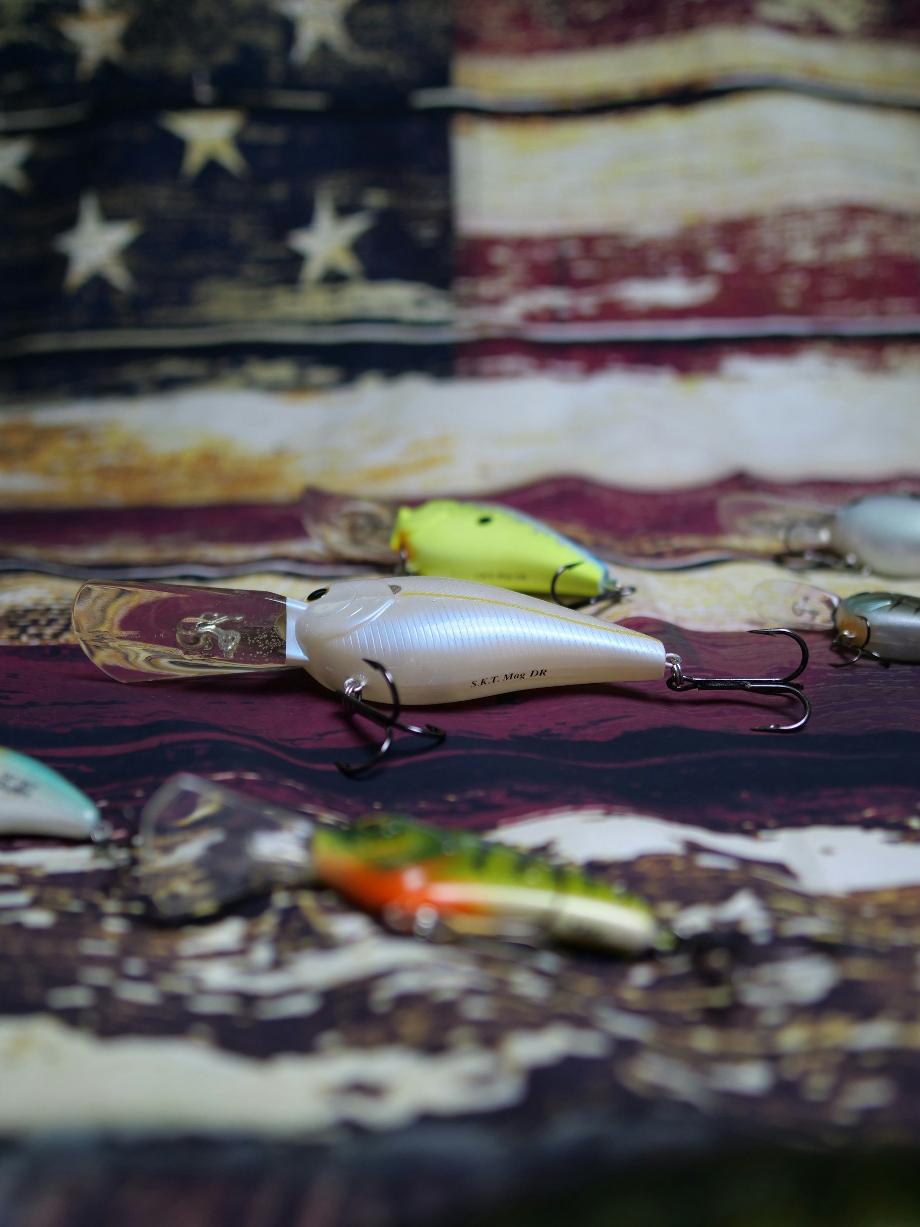 Close-up of several fishing lures placed on a surface with an American flag design in the background.