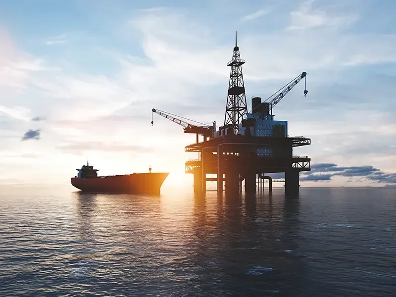 Oil platform with a ship nearby during sunset in the ocean.