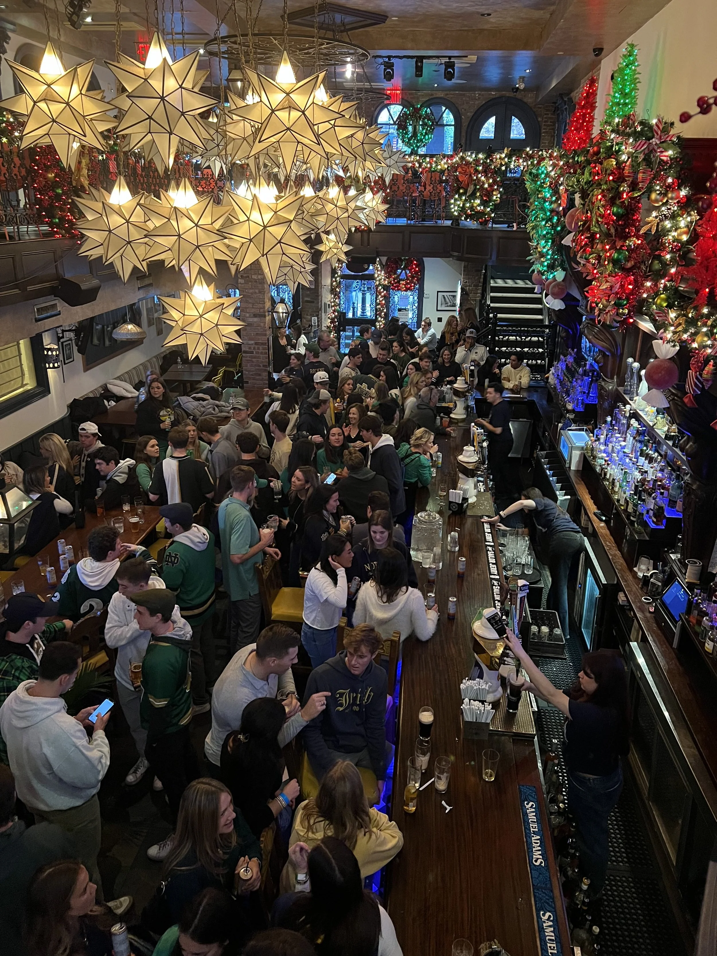 A crowded bar decorated for Christmas with festive ornaments, bright lights, and hanging star-shaped lights.