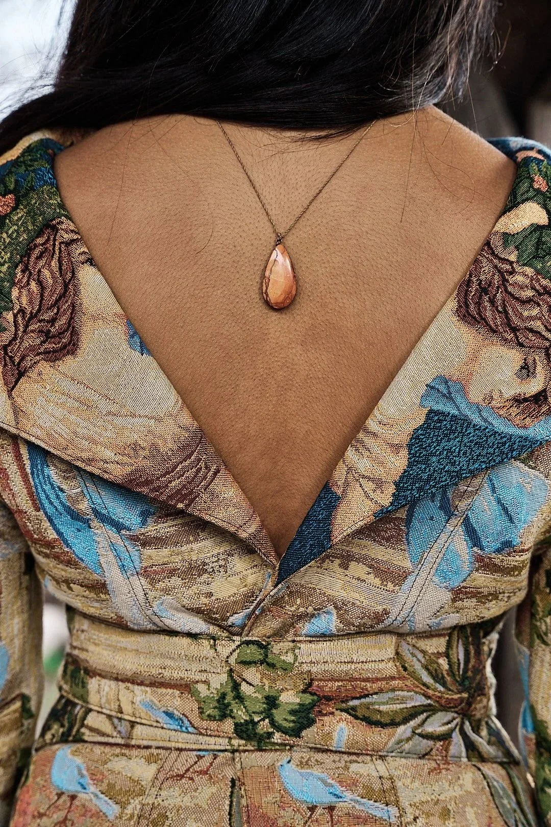 Collier avec pendentif en forme de goutte suspendu autour du cou d'une personne portant une chemise richement brodée de motifs floraux. . Photo prise par Maison Toki pour Maison Préfontaine.