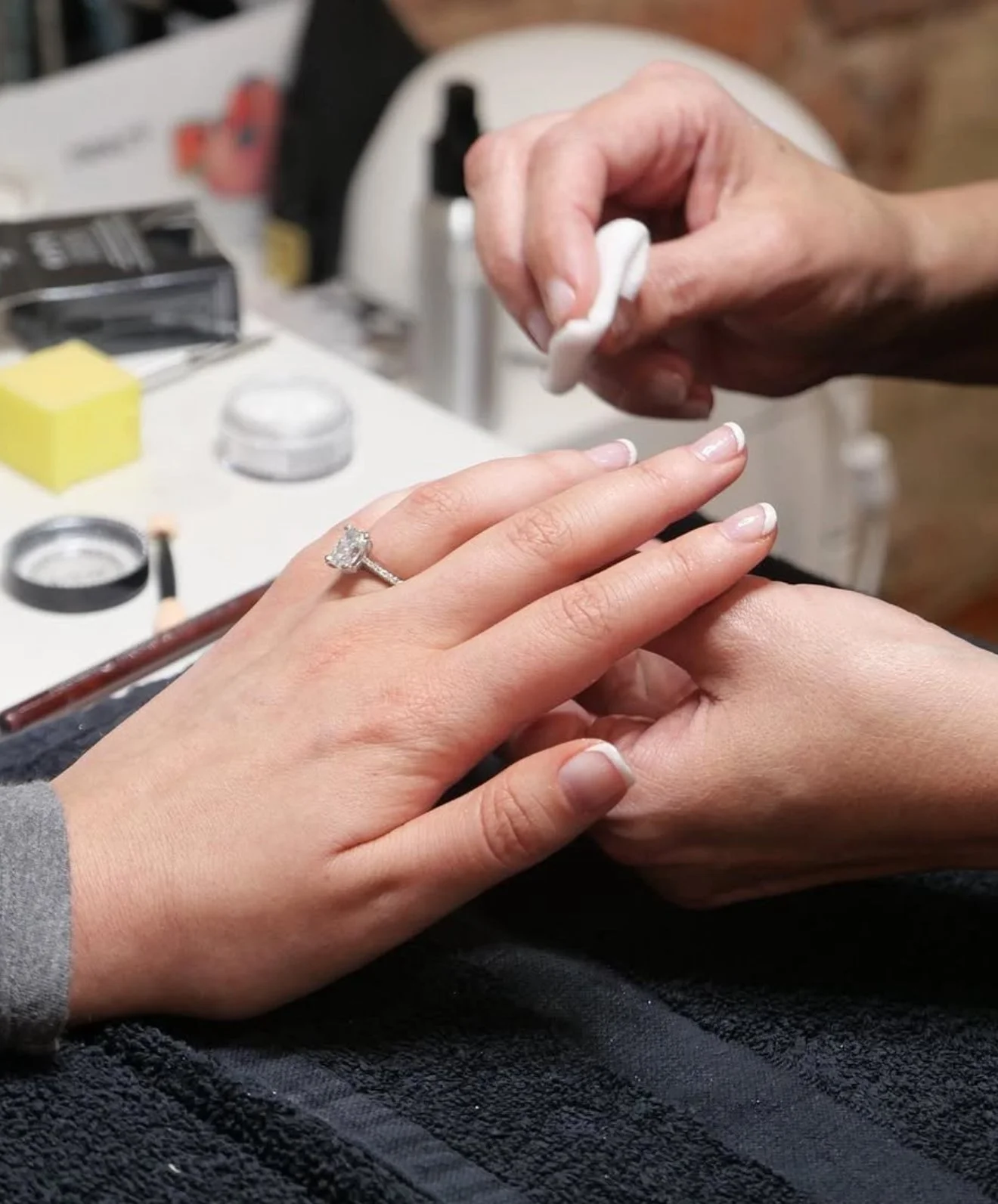 A person getting a manicure at Lark and Sparrow, with a focus on the hand wearing an engagement ring on the ring finger.