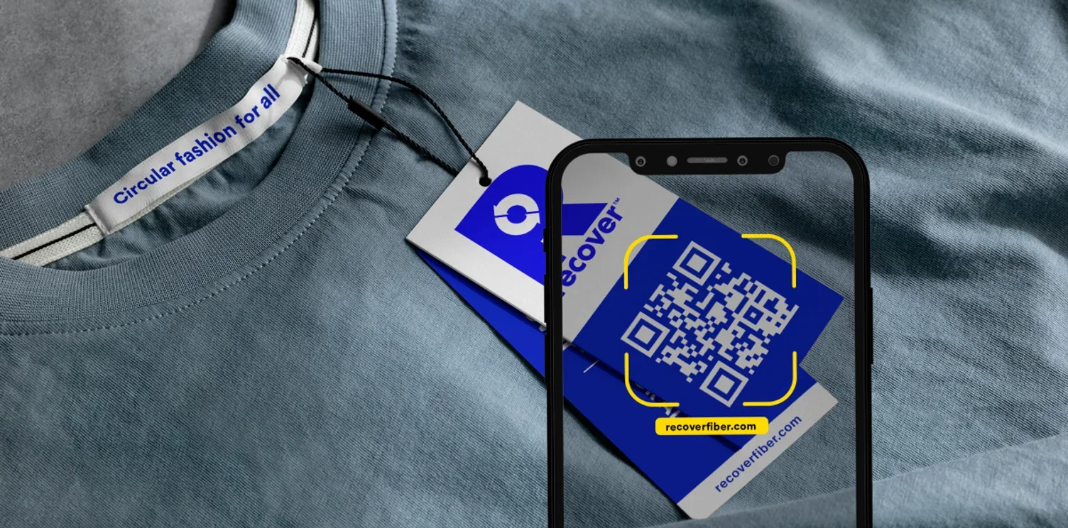 A smartphone scanning a QR code on clothing tags, with a clothing tag labeled 'Circular fashion for all' and a website URL recoverfiber.com.