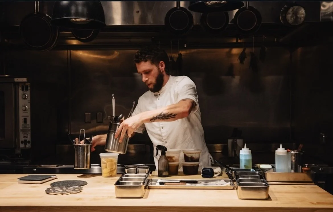 A chef preparing drinks behind a wooden counter in a professional kitchen.