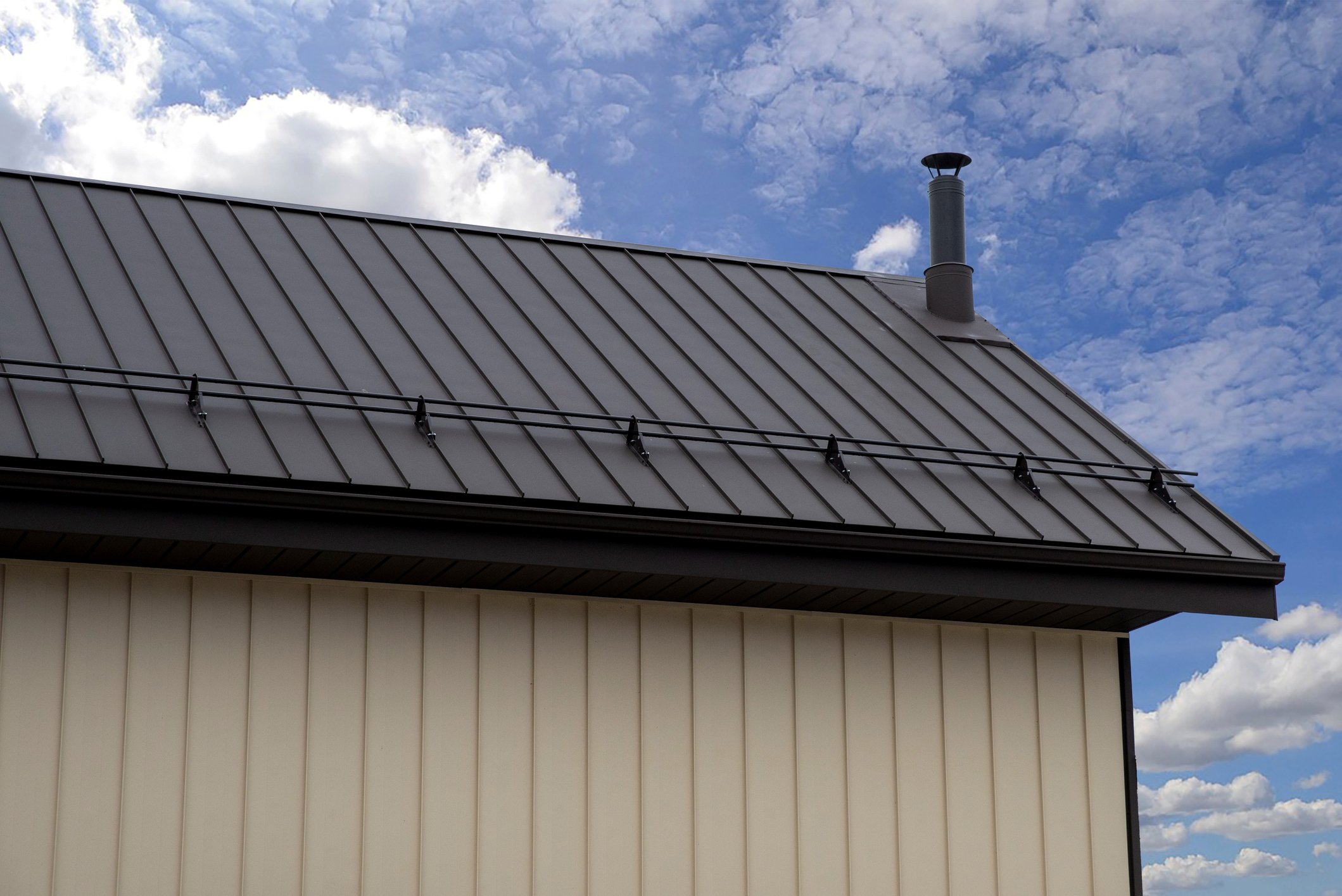 View of house roof with metallic panels, a chimney, power lines, and a partly cloudy sky.
