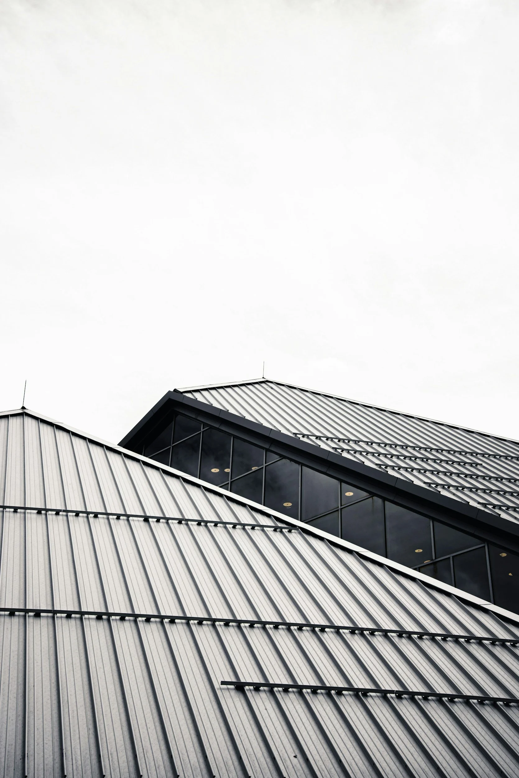 Modern building with a sloped metal roof and large glass windows, under an overcast sky.