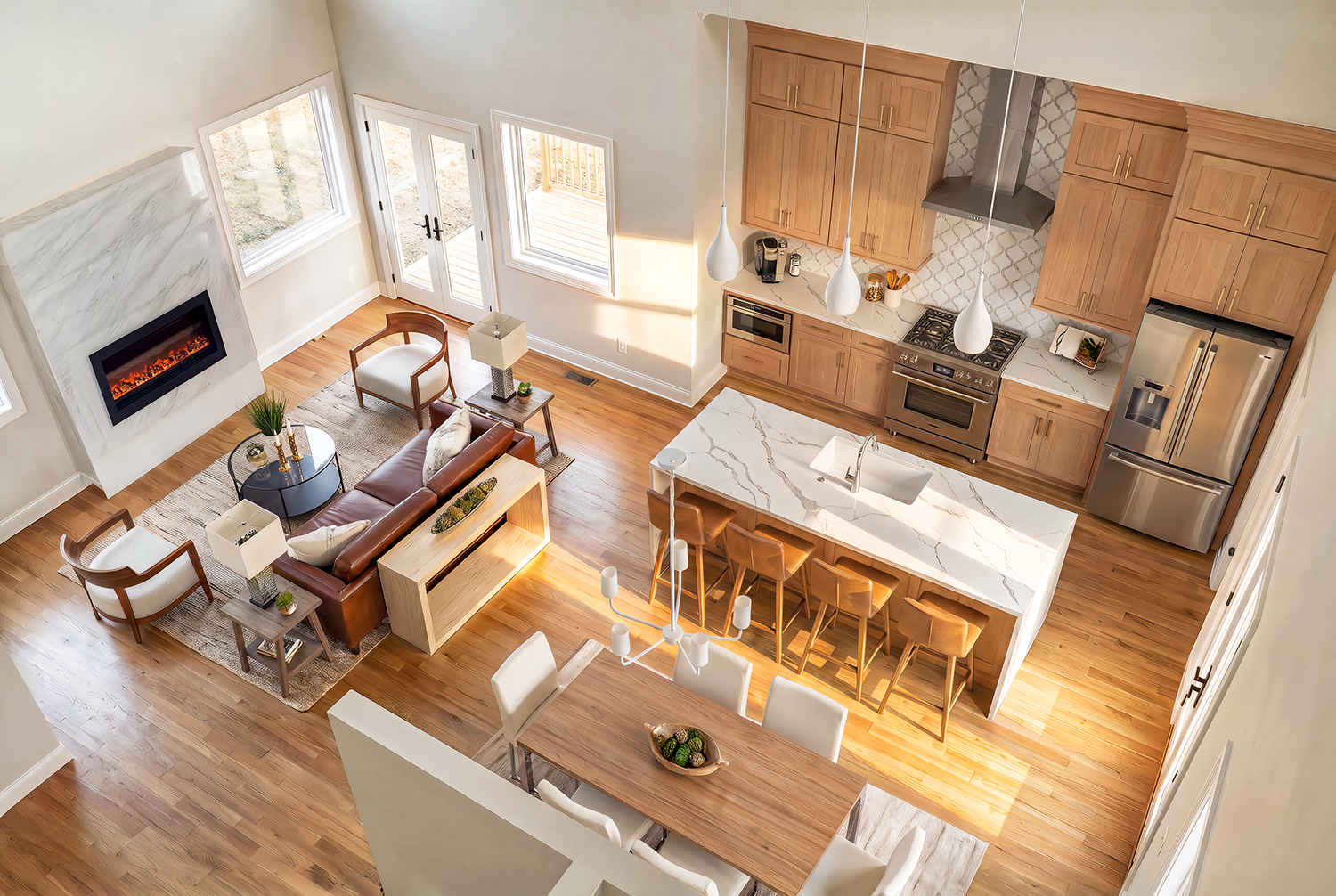 An open-concept living room and kitchen with hardwood floors, a leather sofa, armchairs, a fireplace, a kitchen island with barstools, and modern appliances.