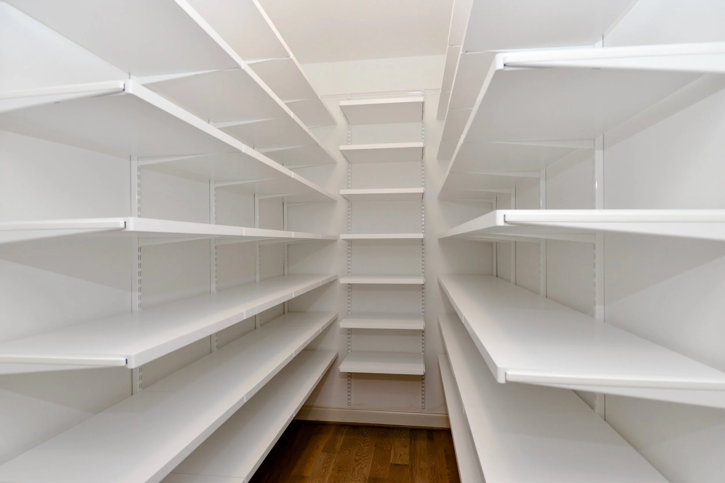 Empty white built-in closet with multiple shelves and a wooden floor.