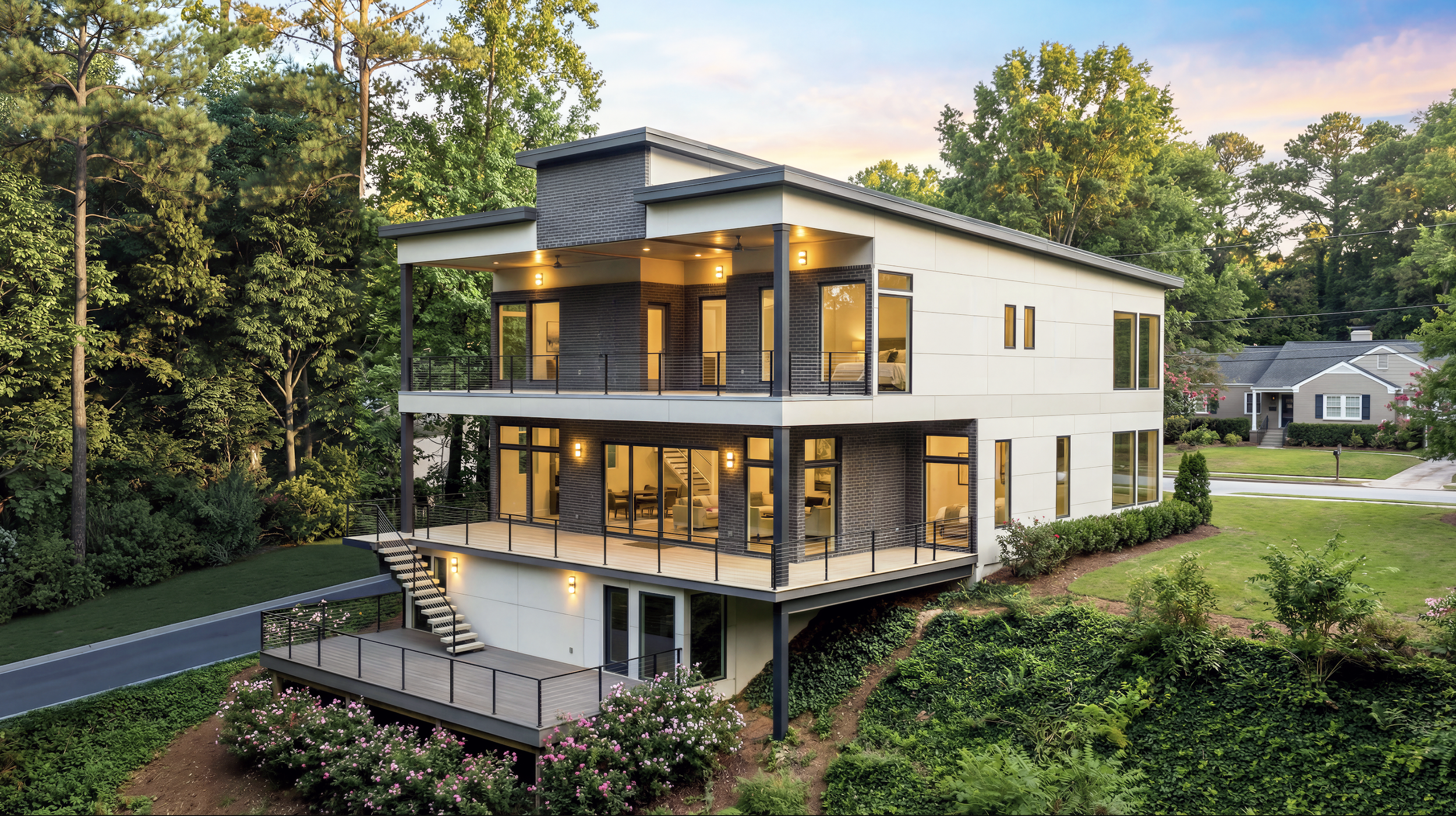 Modern white and black multi-story house with large windows, a front porch with steps, and a spacious driveway, surrounded by a well-maintained lawn and trees.