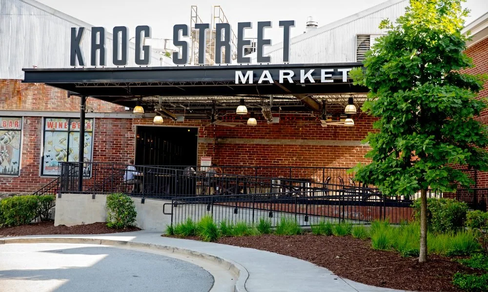 Krog Street Market entrance with large sign, brick walls, and greenery in front on a sunny day.