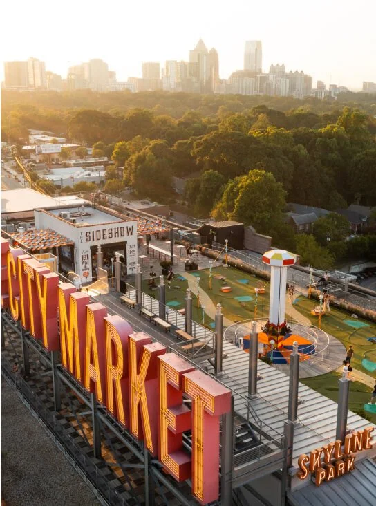 A rooftop park at Ponce City Market with games, rides, and a city skyline in the background at sunset.