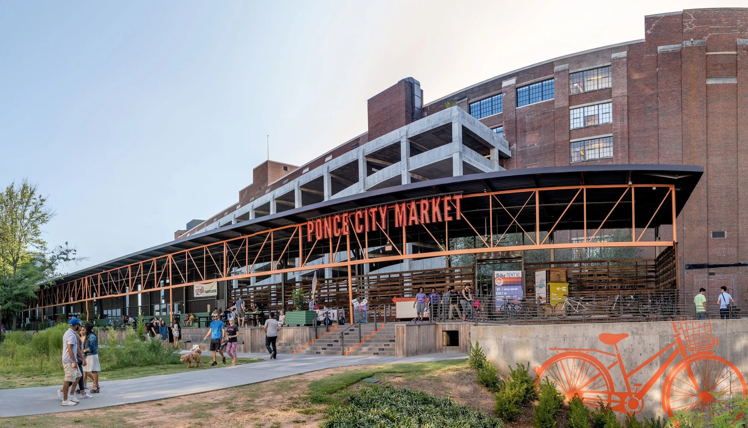 People walk near the entrance of Ponce City Market, a large brick building with an orange sign and covered outdoor area.