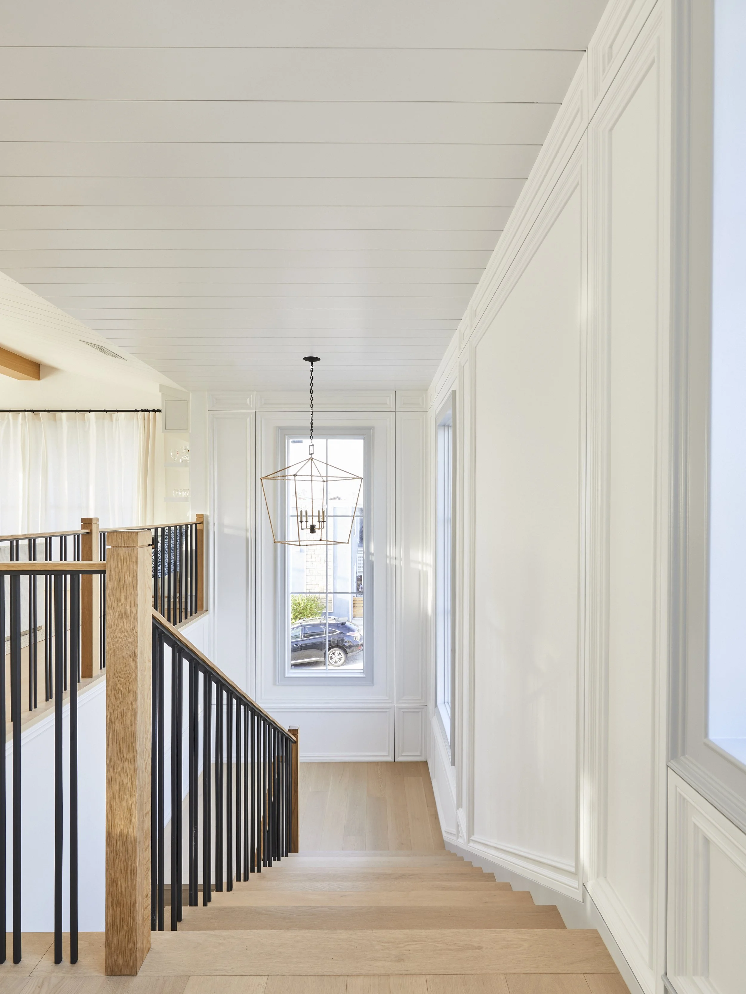 Modern interior staircase with wooden steps and black metal railing, white paneled walls, and a geometric pendant light.