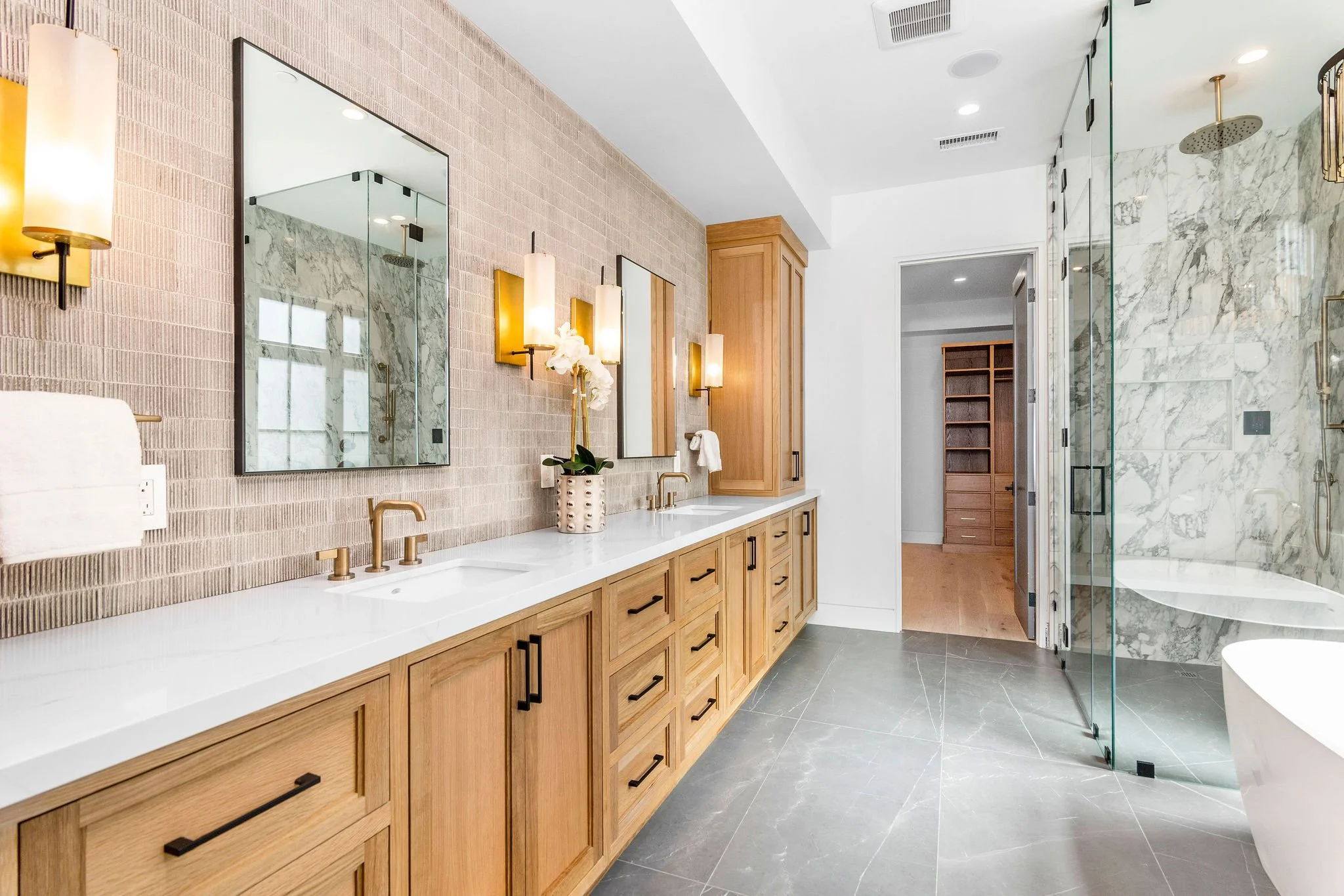 Modern bathroom with double vanity, wooden cabinets, glass shower enclosure, and marble tile accents.