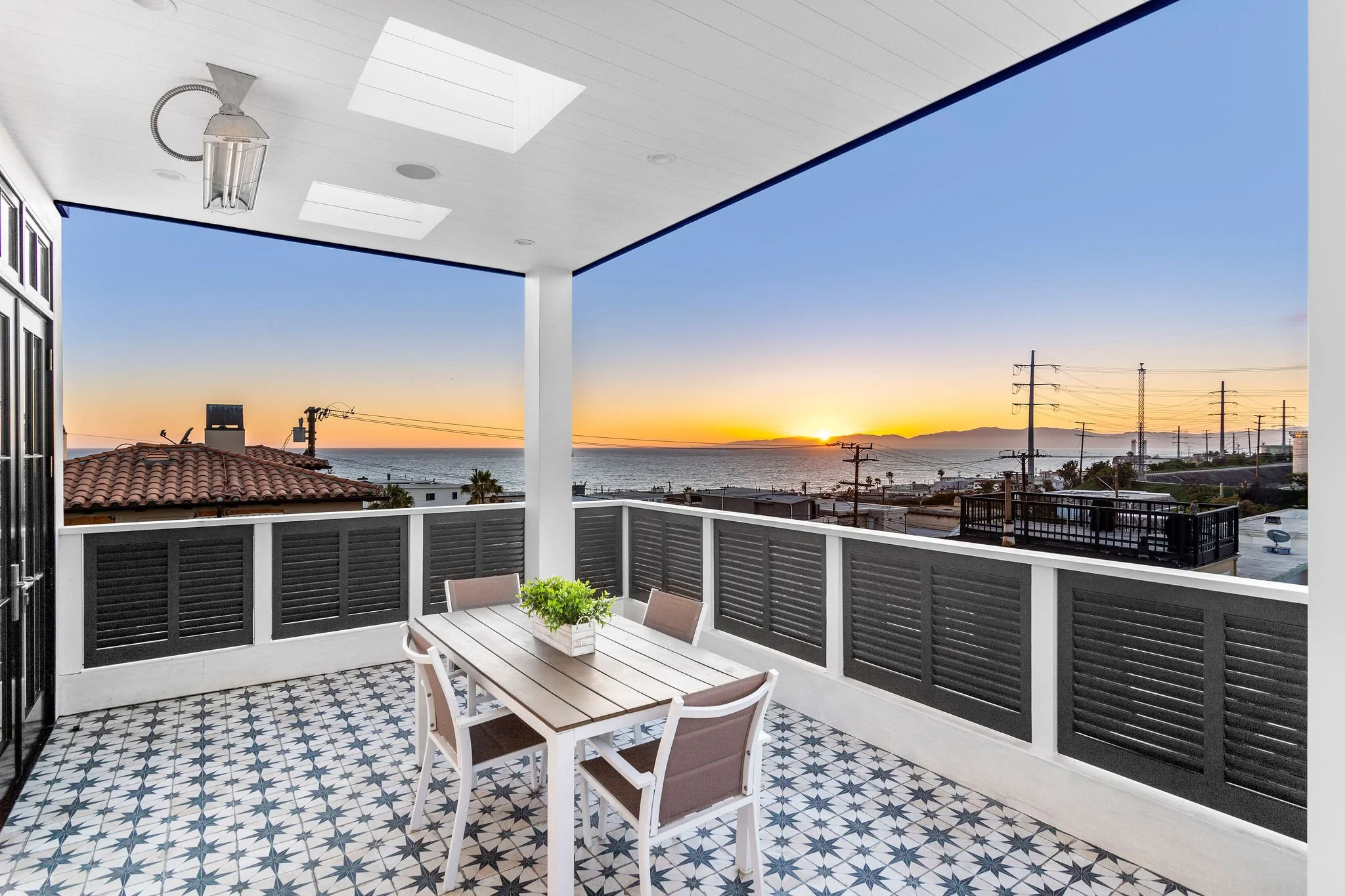 Outdoor balcony with dining table, chairs, and ocean view at sunset