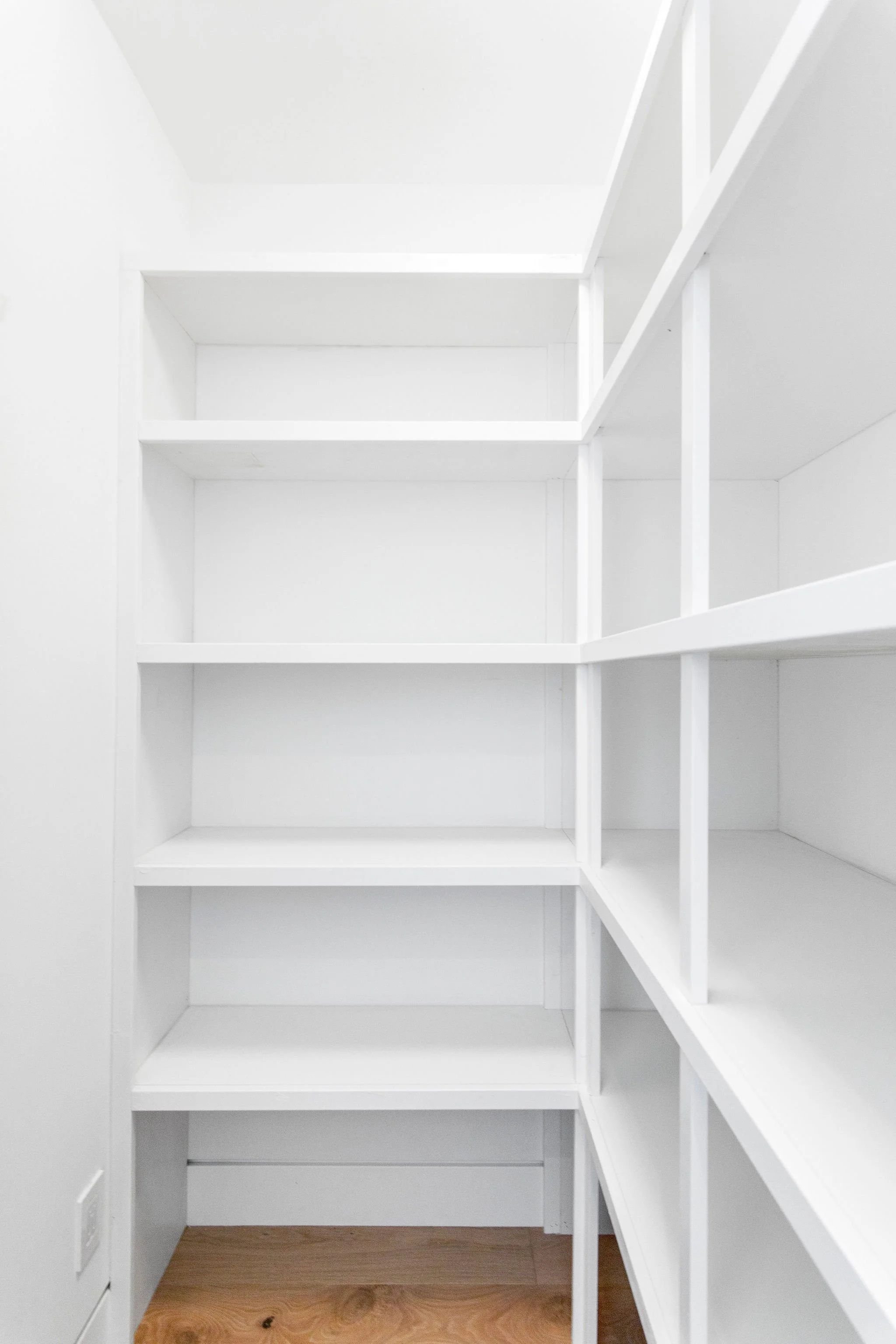 Empty white shelving units in a small room with wooden flooring.